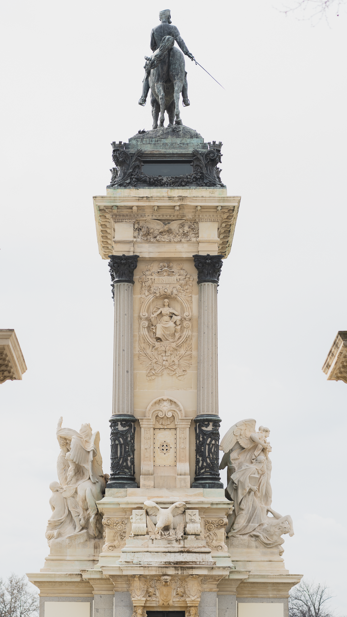 Detail of the Alfonso XII monument column in El Retiro Park, Madrid, with winged marble figures and a bronze equestrian statue