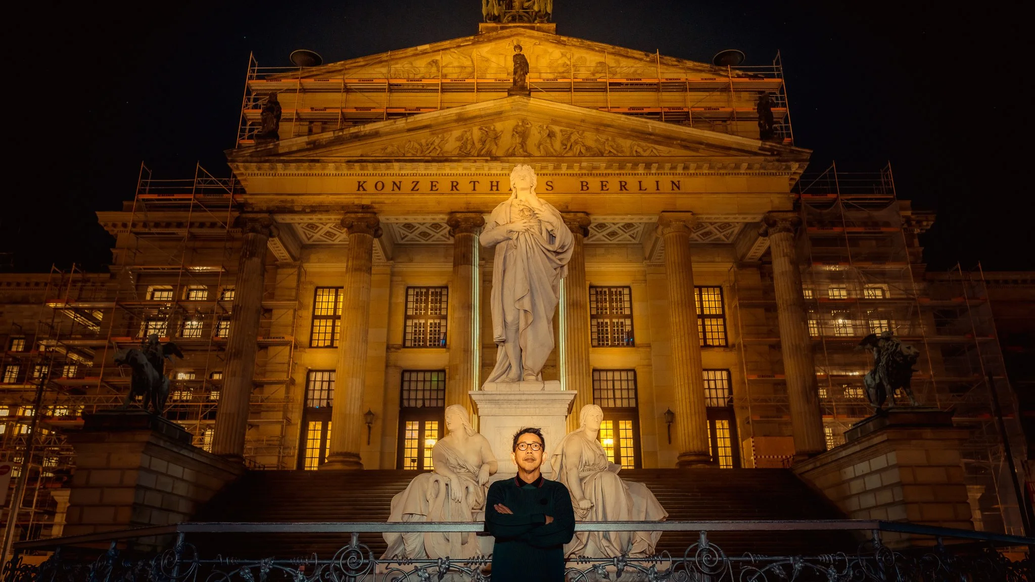 Herwin Gunawan stands in front of the Schiller Monument and the warmly illuminated façade of Konzerthaus Berlin at night