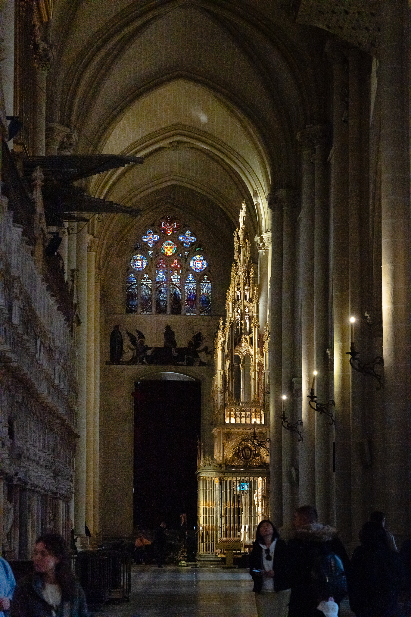 Carved marble and gilt screen at the rear of the choir enclosure in Toledo Cathedral, beneath a ribbed star vault, with stained glass windows on either flank