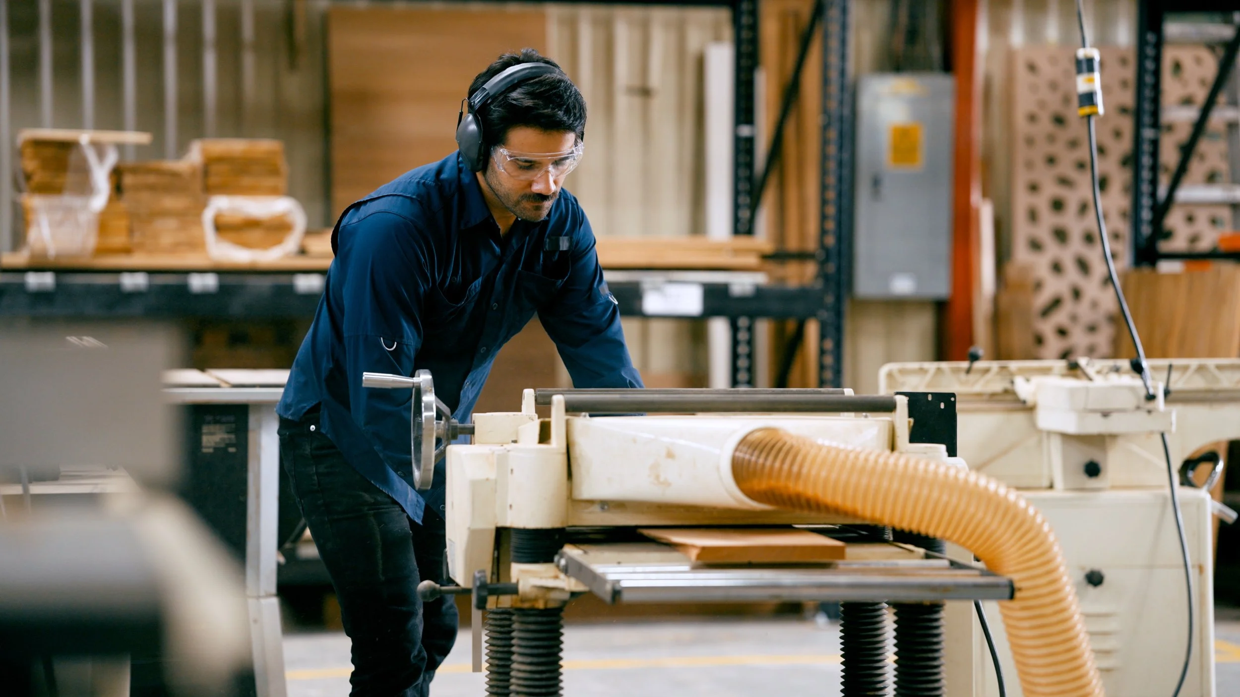 A man wearing safety goggles and headphones operating woodworking equipment in a workshop.