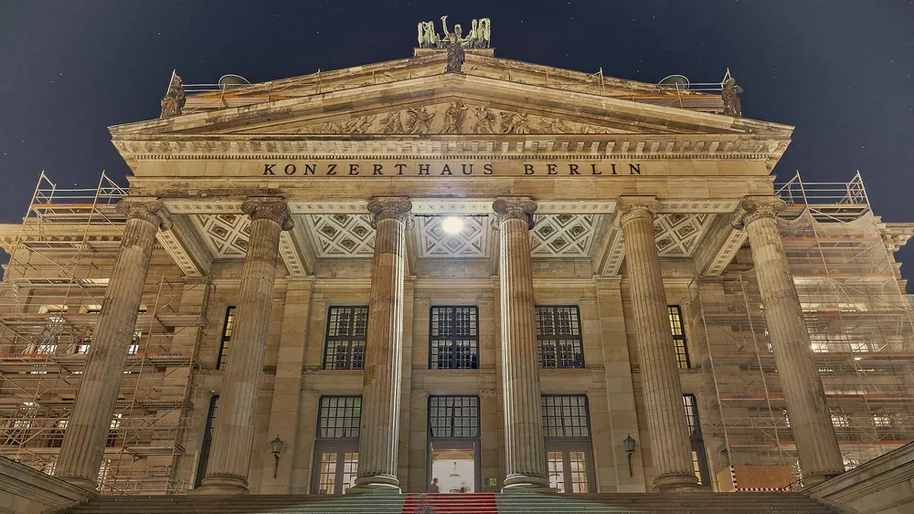 Upward view of the Konzerthaus Berlin portico, showing six fluted columns, a geometrically patterned ceiling, and sculpted reliefs in the pediment.