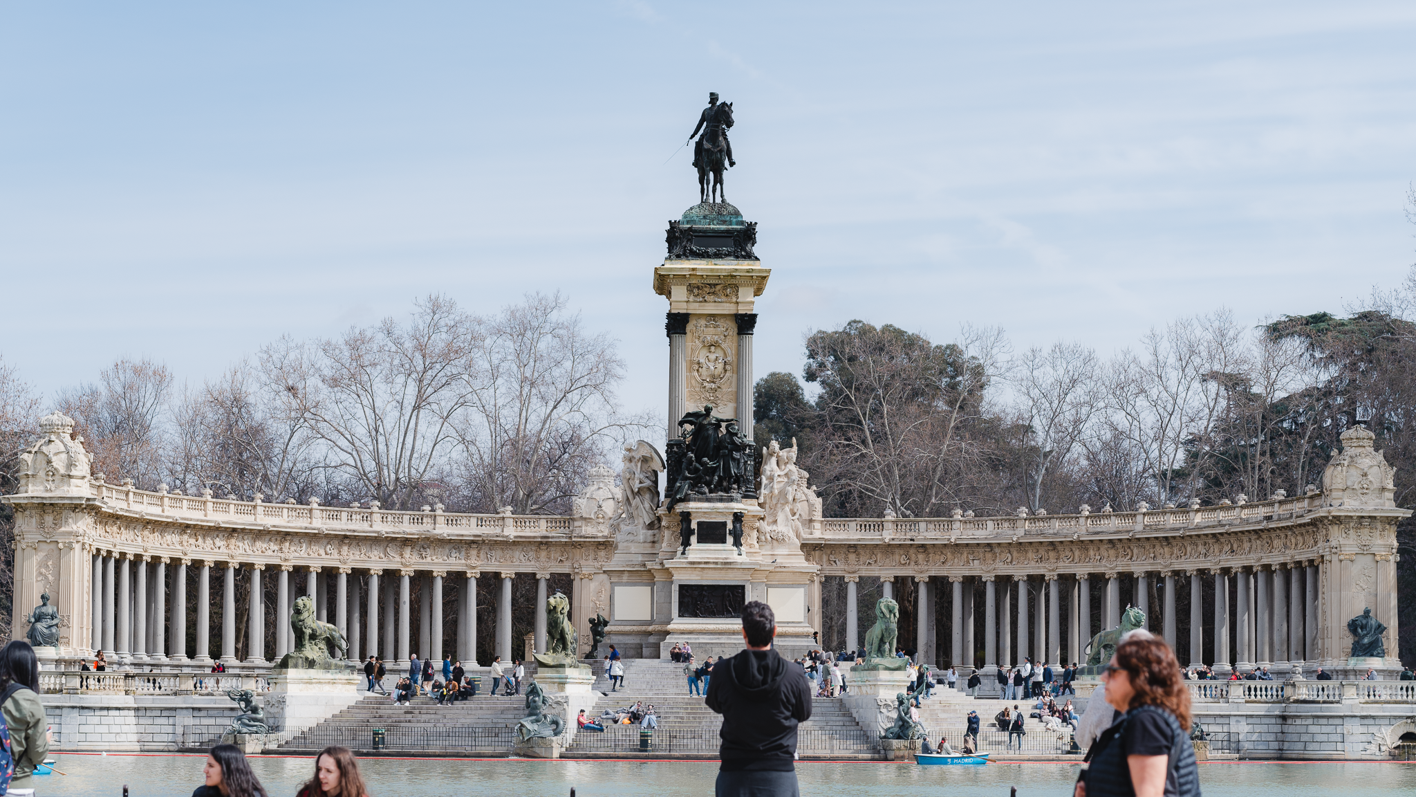 Curved colonnade and bronze equestrian statue of the Alfonso XII monument above the boating lake in El Retiro Park, Madrid