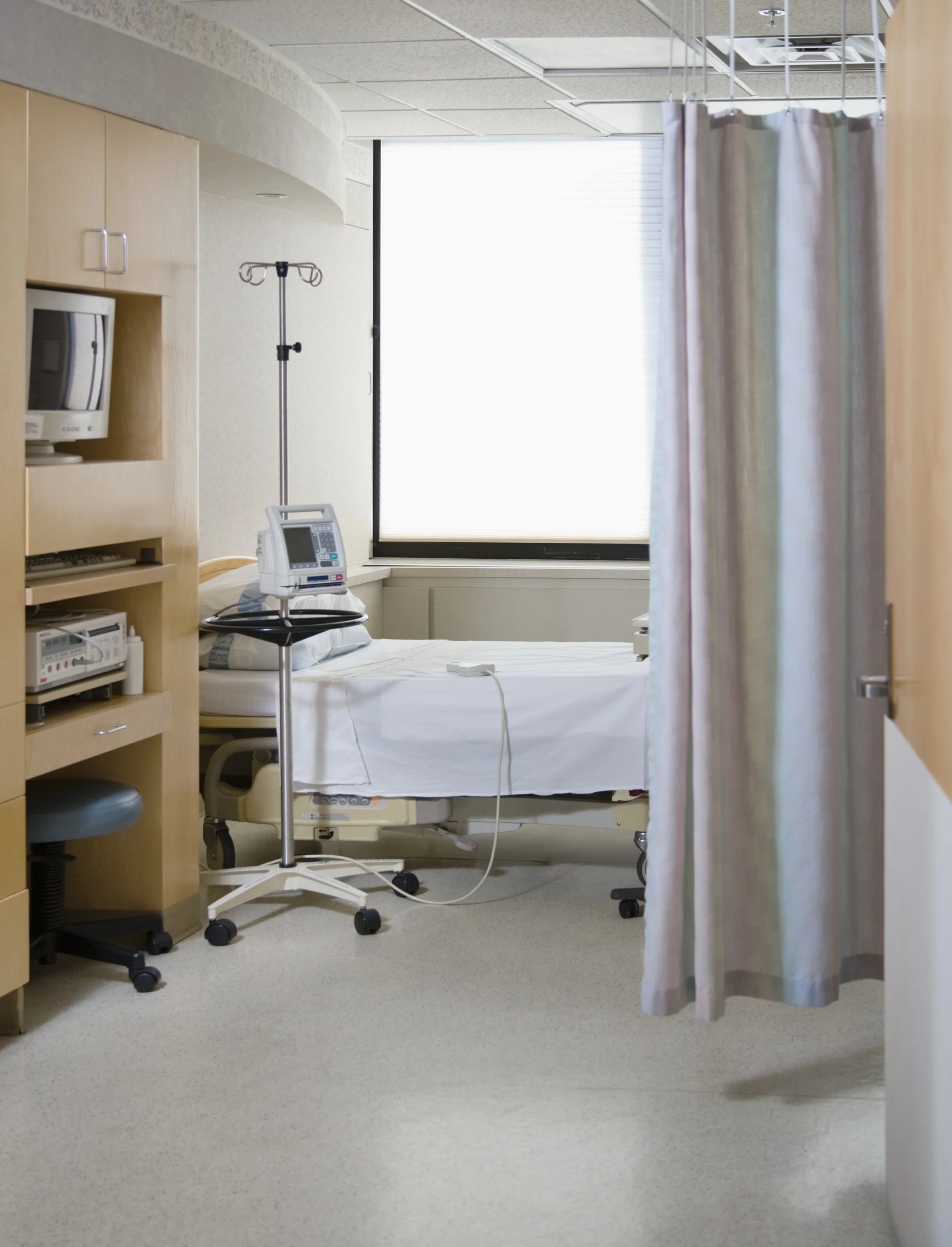 Hospital room with a bed, medical equipment, an IV stand, a telephone, a computer, a curtain, and a window with blinds.