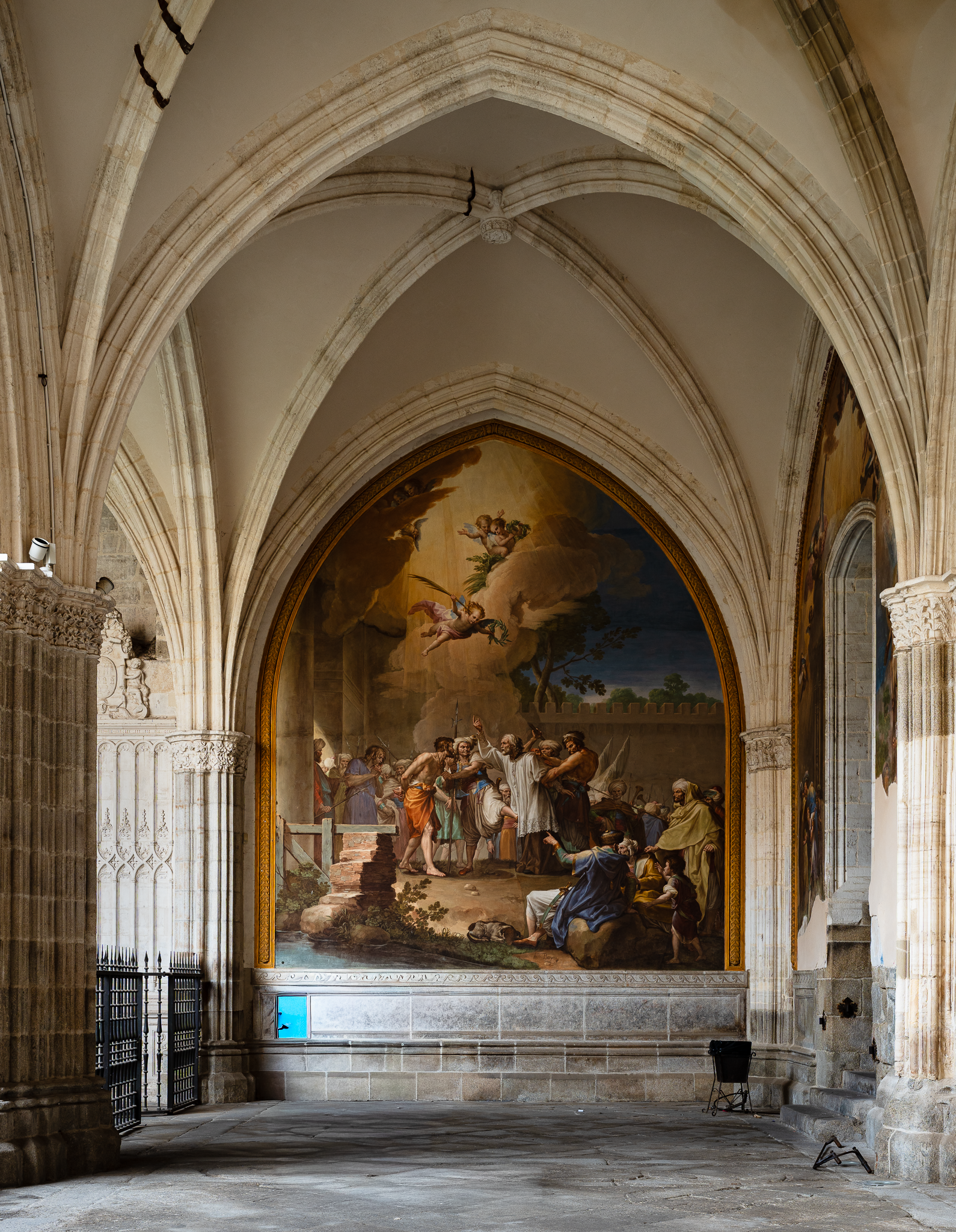 Cloister bay in Toledo Cathedral with a large painted mural filling the pointed arch, lit by indirect daylight beneath a pale ribbed vault