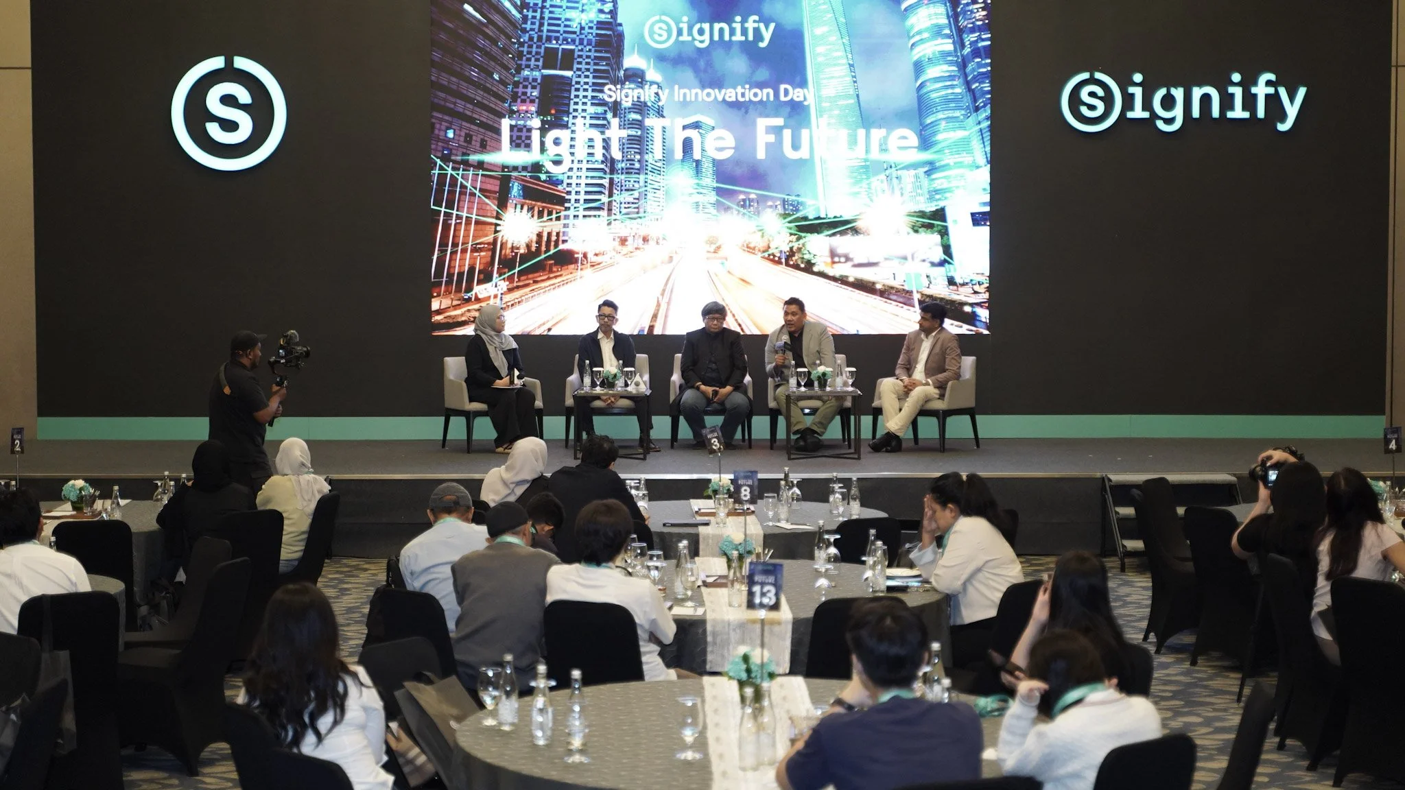Panel speakers seated on stage at Signify Innovation Day with the Light The Future event screen behind them.