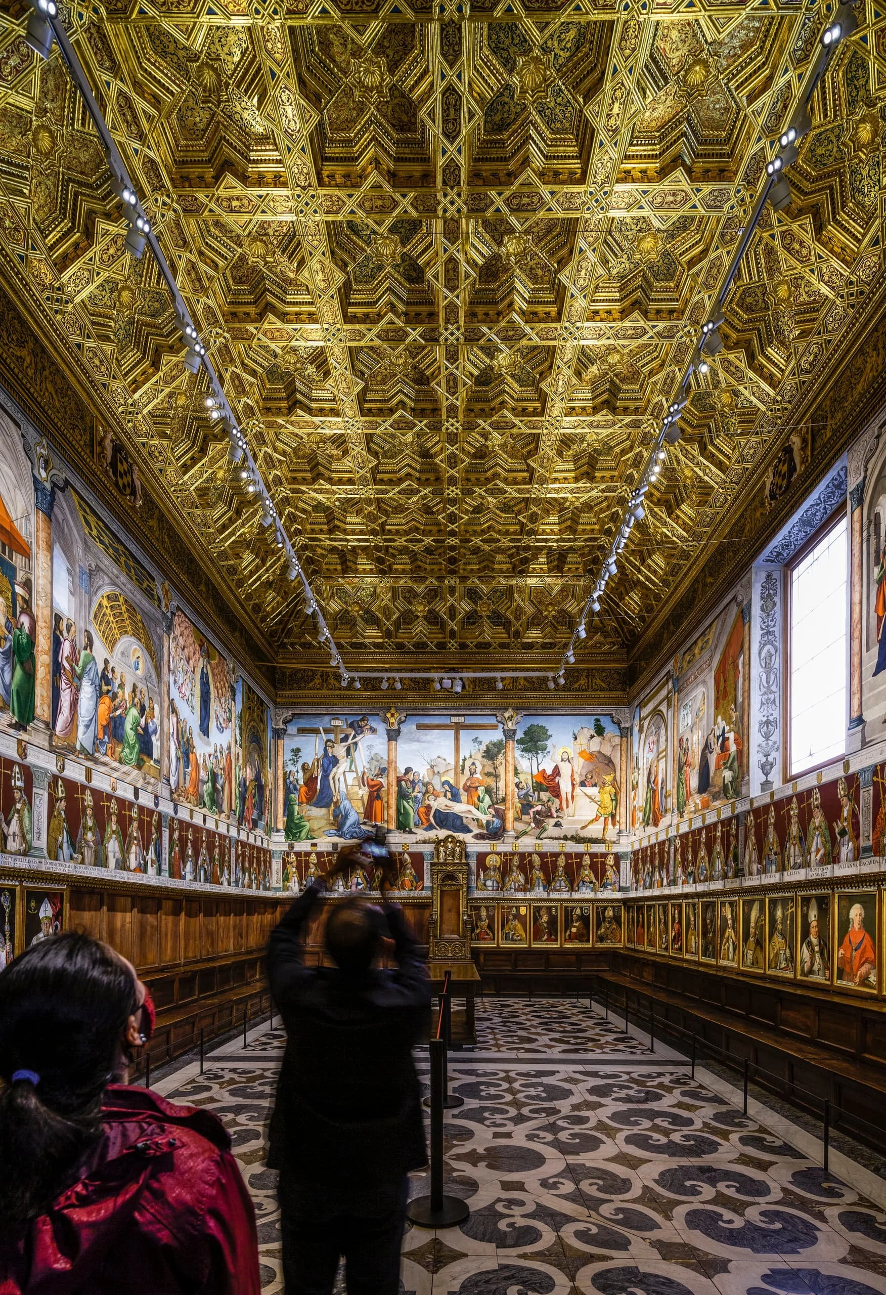 Toledo Cathedral’s chapter house, with a gilded geometric ceiling, suspended lighting tracks, wall paintings and rows of archbishops’ portraits.