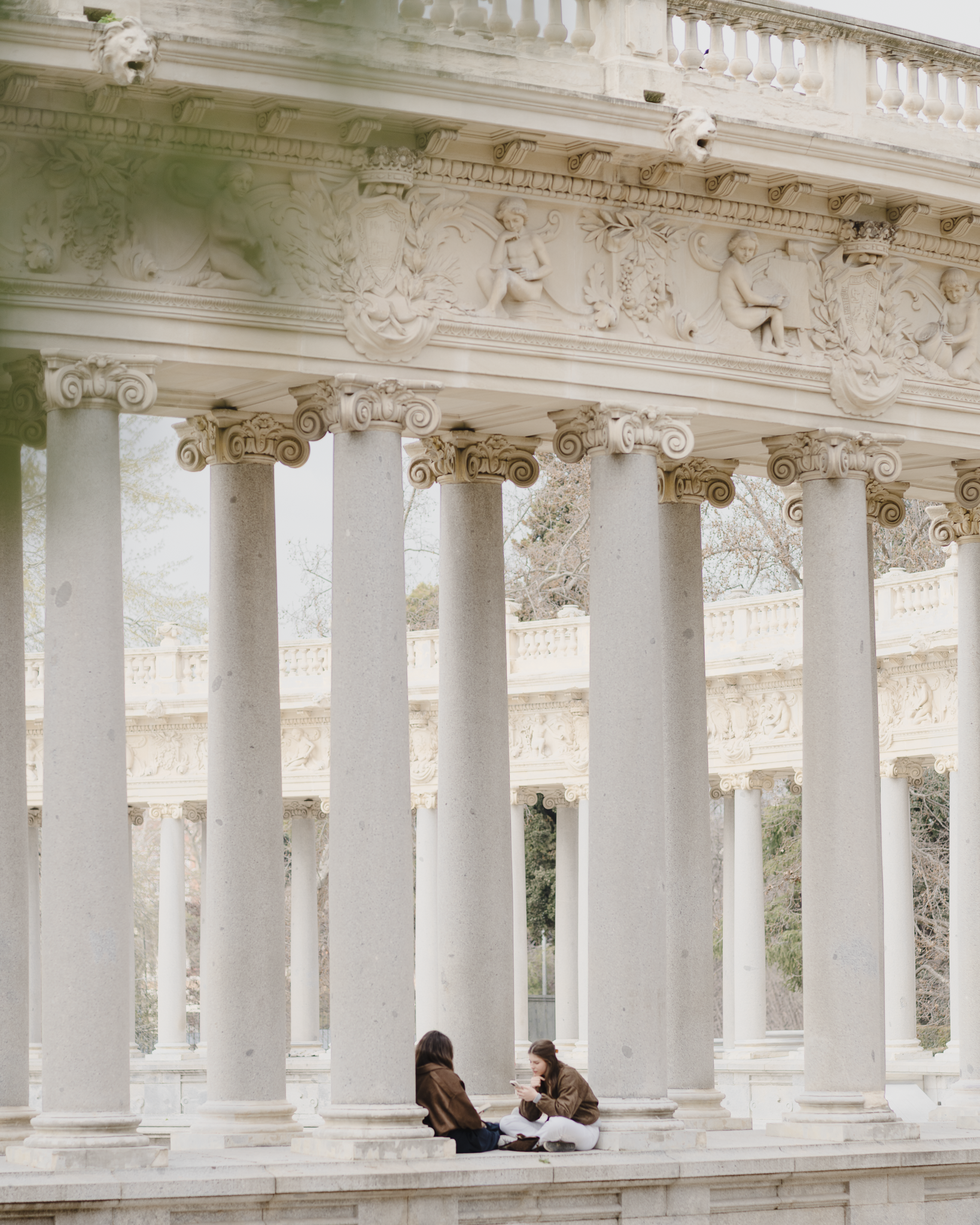 Two visitors sitting beneath the Ionic colonnade of the Alfonso XII monument in El Retiro Park, Madrid