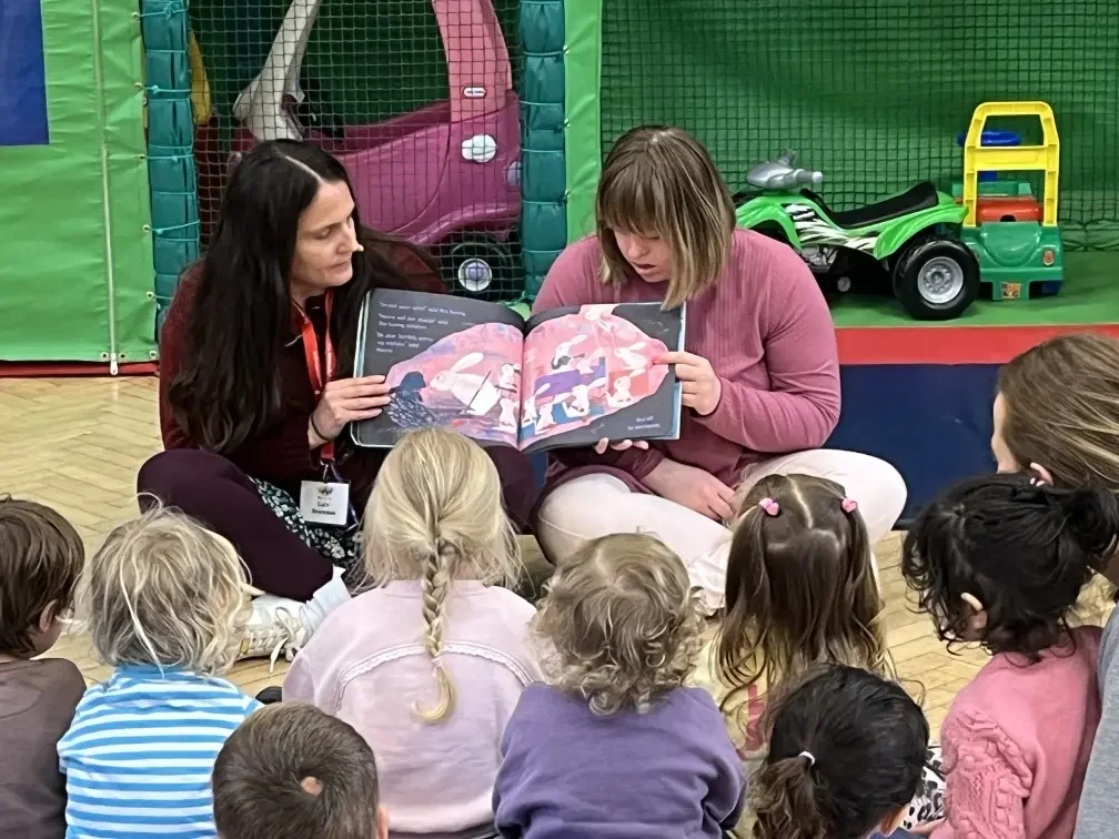 Oasi See and Know - Lucy reading a picture book to a group of children in a play area with toys.
