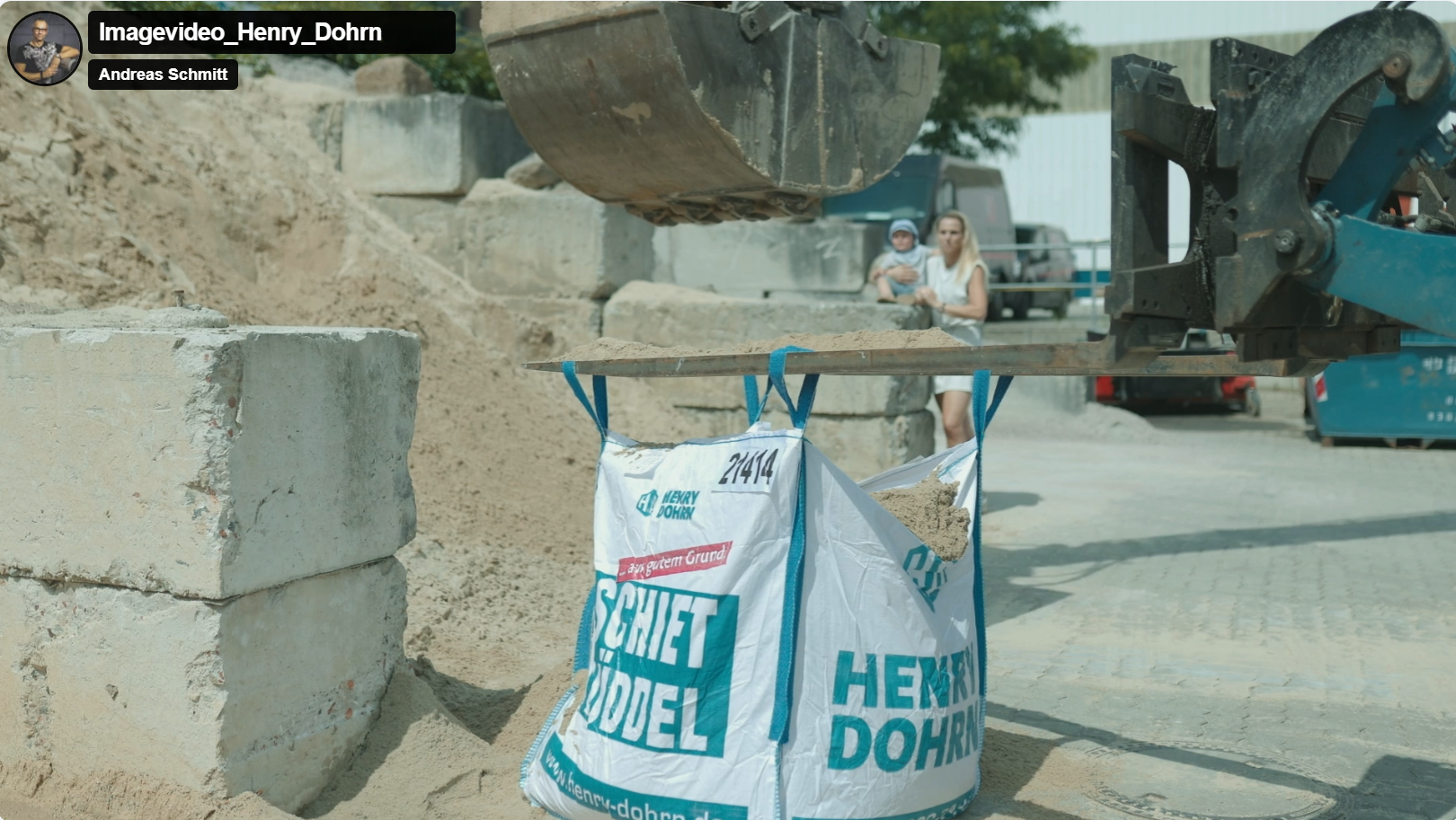 Bauarbeiter beim Bau einer Mauer mit Gummischaufel und Zement, Sand und Steine auf einer Baustelle, im Hintergrund zwei Frauen und ein Kind, Fahrzeuge und Container