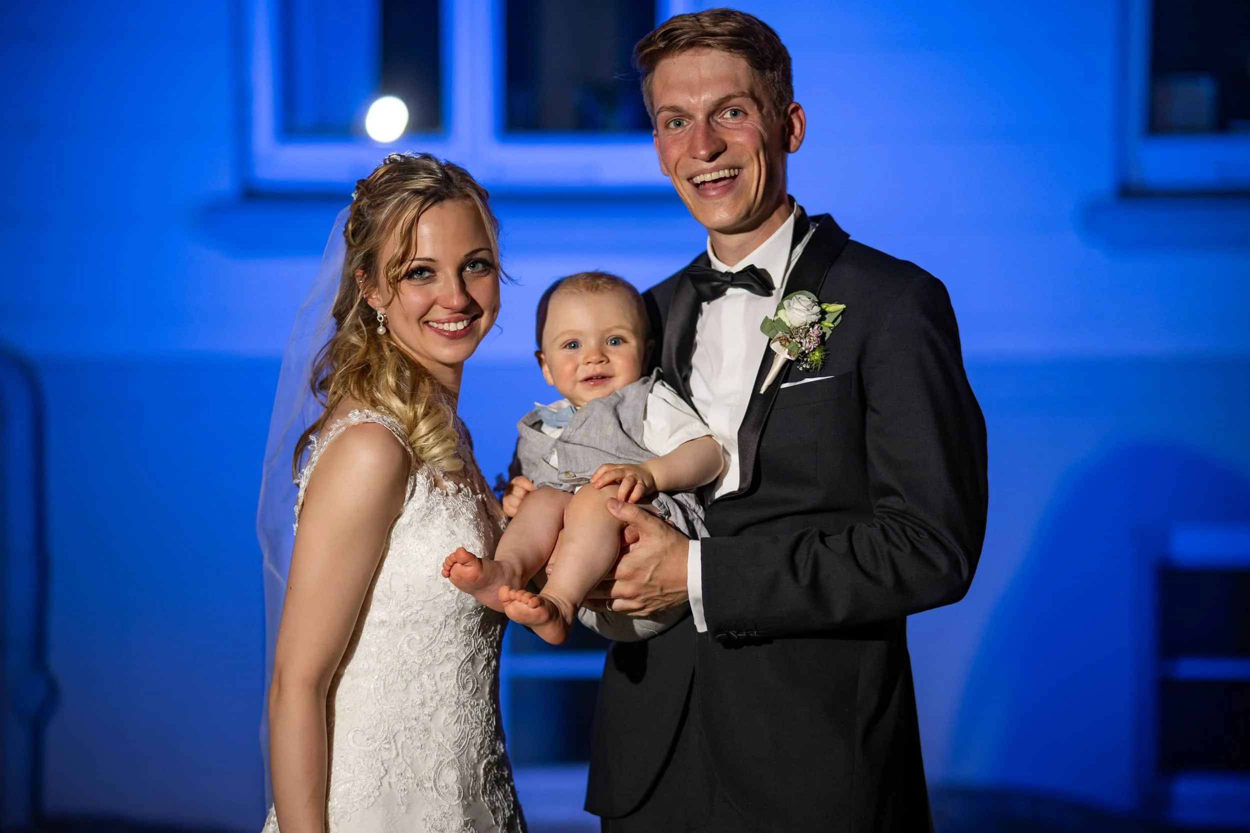 Brautpaar mit ihrem Baby vor einer blauen Kulisse.jpg