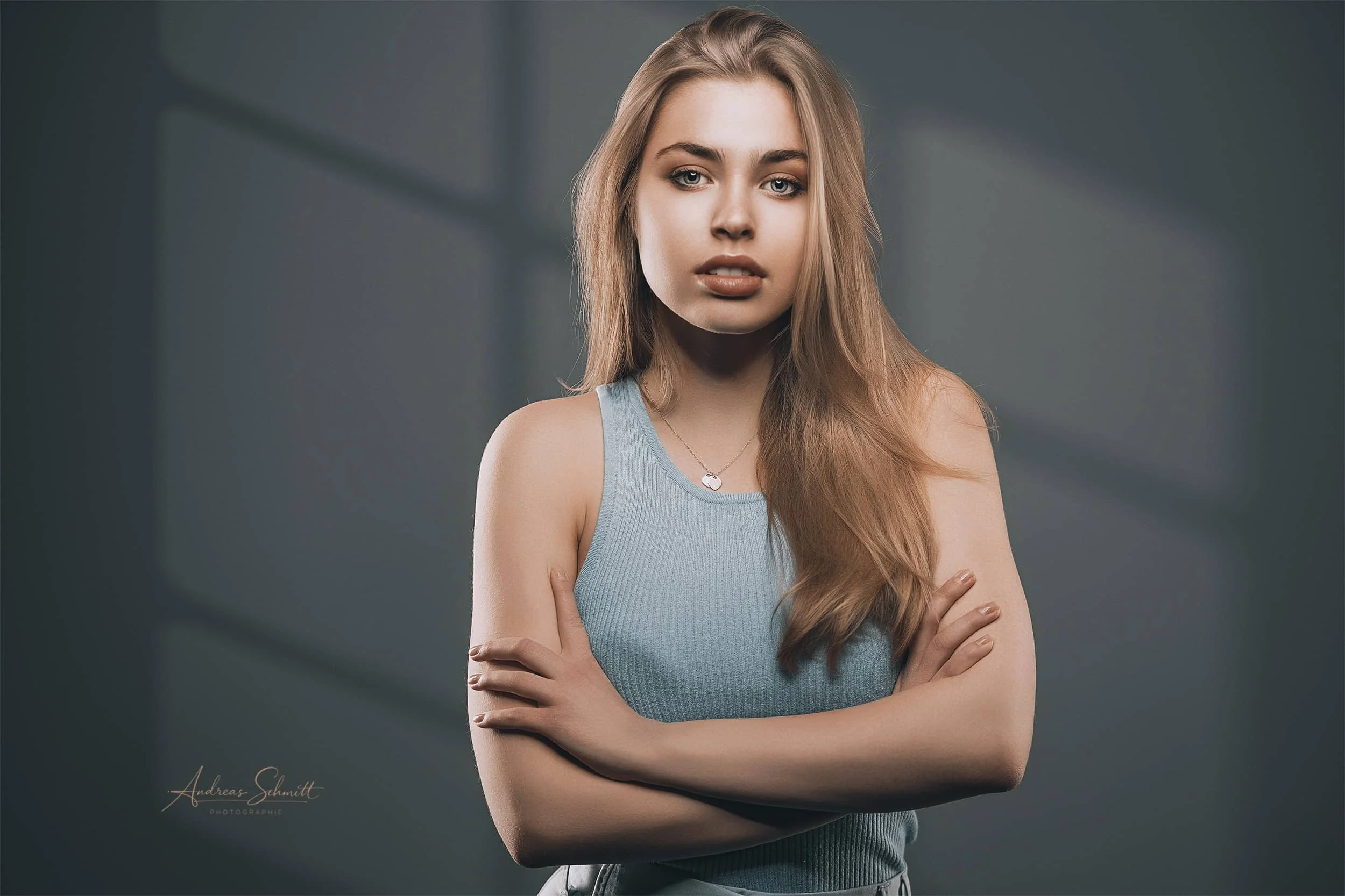 Junge Frau mit lockigem, langem, hellbraunem Haar trägt ein hellblaues Rippentop und blickt ernst in die Kamera, verschränkt die Arme vor der Brust.