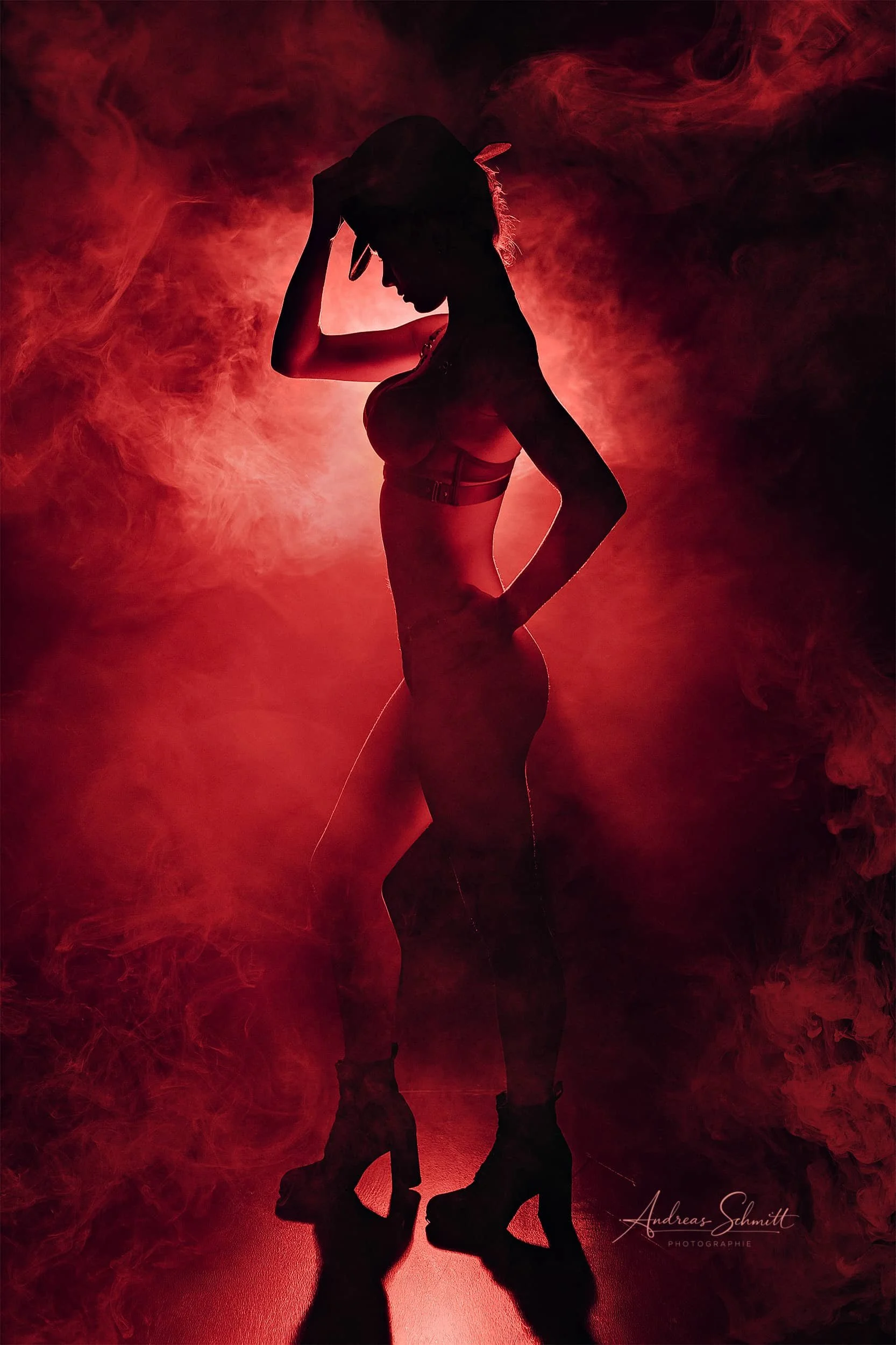 Silhouette einer Frau mit Cowboyhut und High Heels vor rotem Rauchhintergrund.