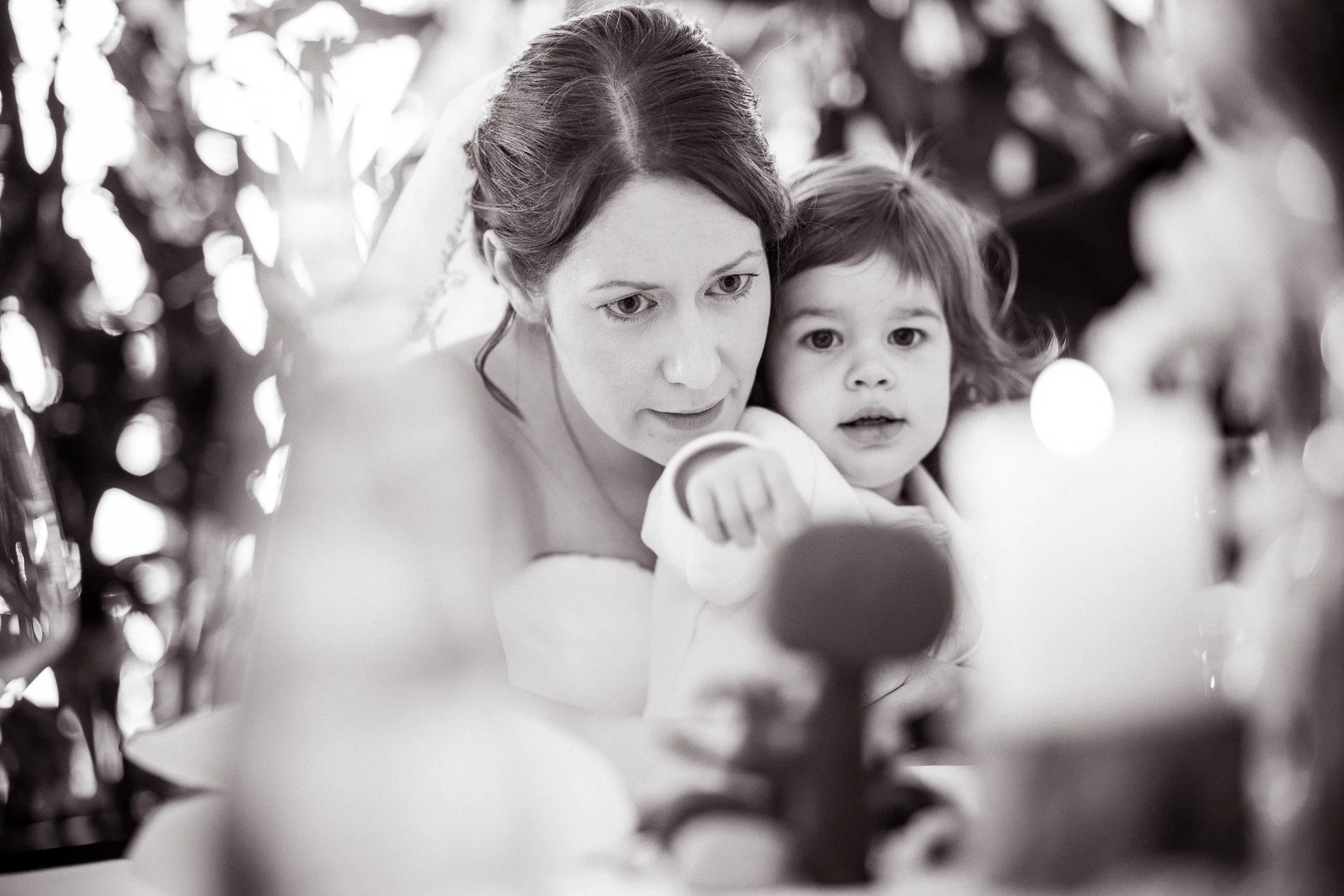 Schwarz-weiß-Foto einer Frau und eines kleinen Mädchens, die zusammen spielen oder sich anschauen, umgeben von Blumen oder Pflanzen.