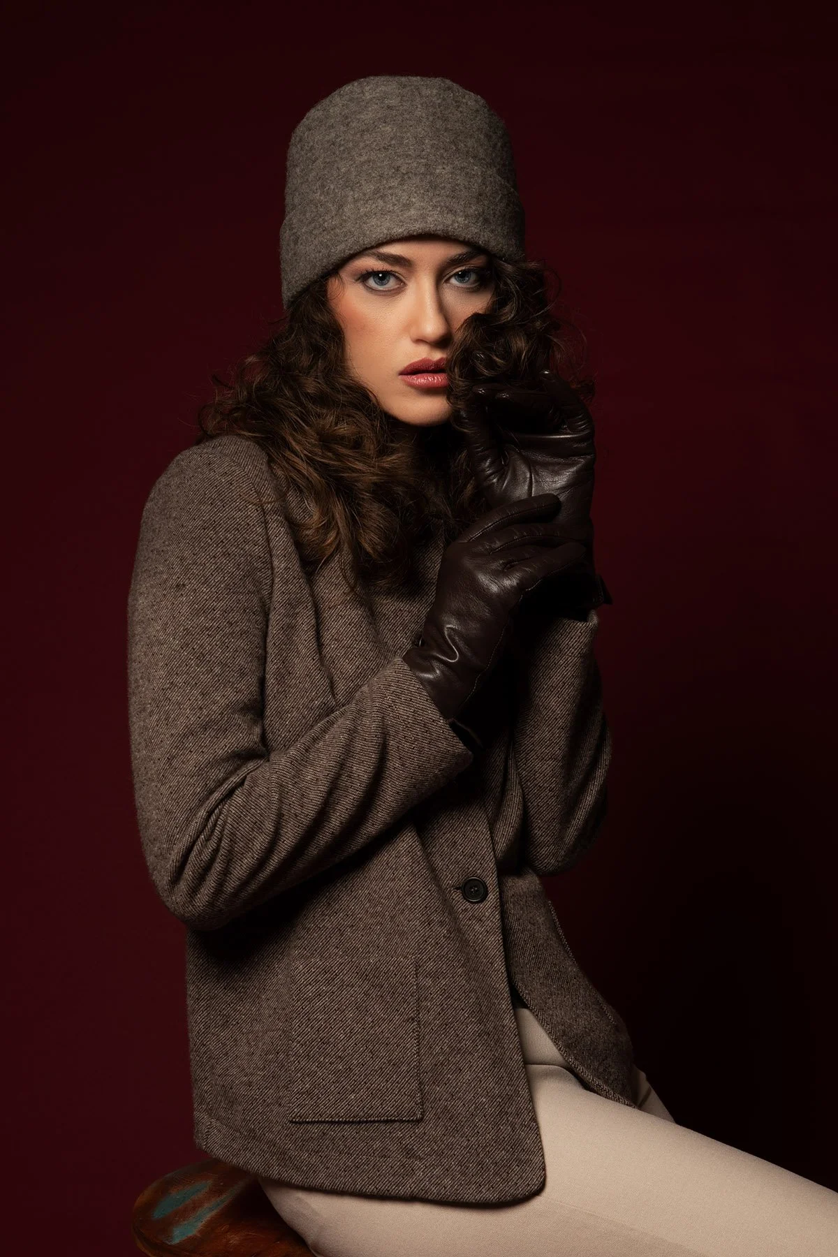 Donna con cappello grigio, giacca beige, scarpe colorate, guanti di pelle scura, sfondo scuro.