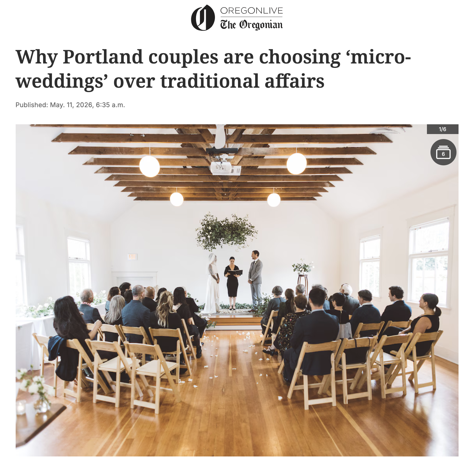 A micro wedding ceremony inside a bright, elegantly decorated room with a wooden ceiling and large windows. The bride and groom are standing at the altar with a officiant. Guests are seated on wooden chairs, watching the ceremony.