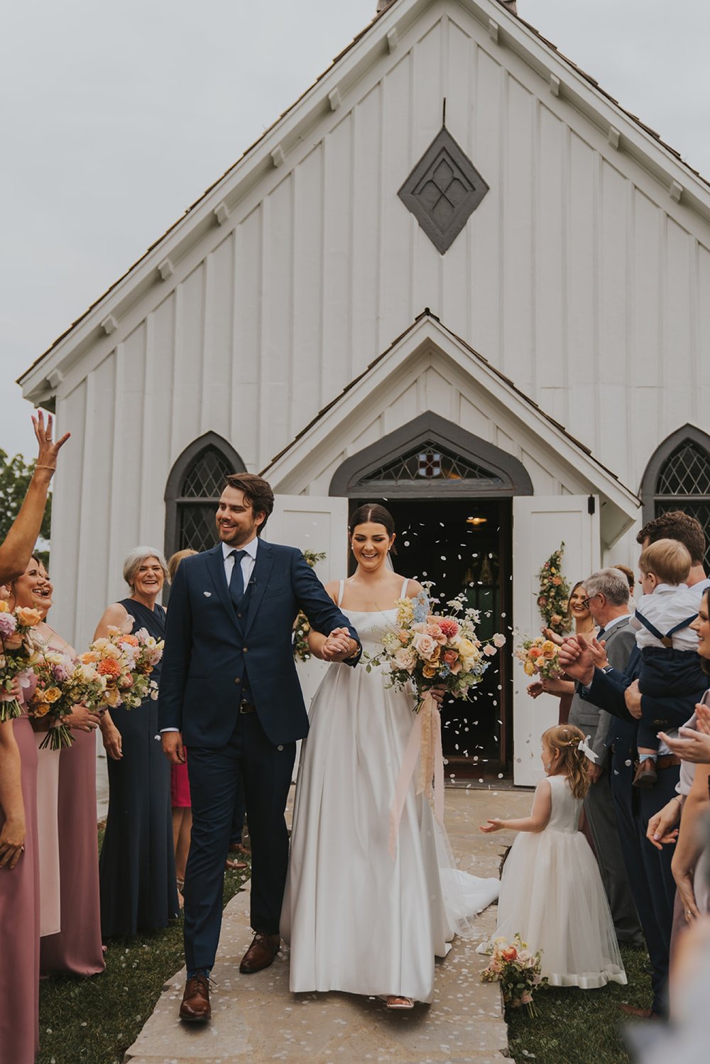 Wedding guests throwing petals over bride and groom outside chapel