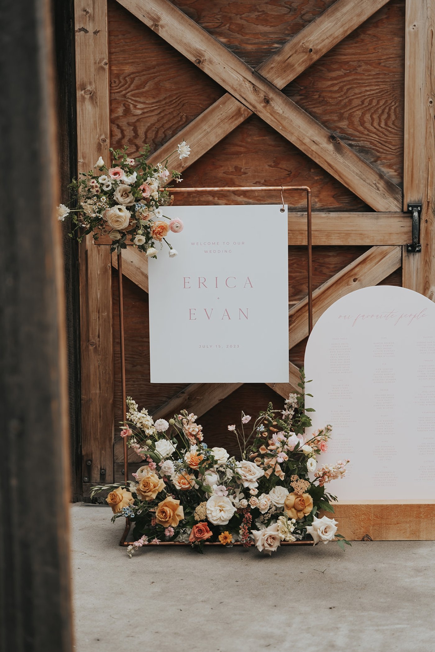 Wedding welcome sign hanging from a rose gold minimalist frame with colorful flowers