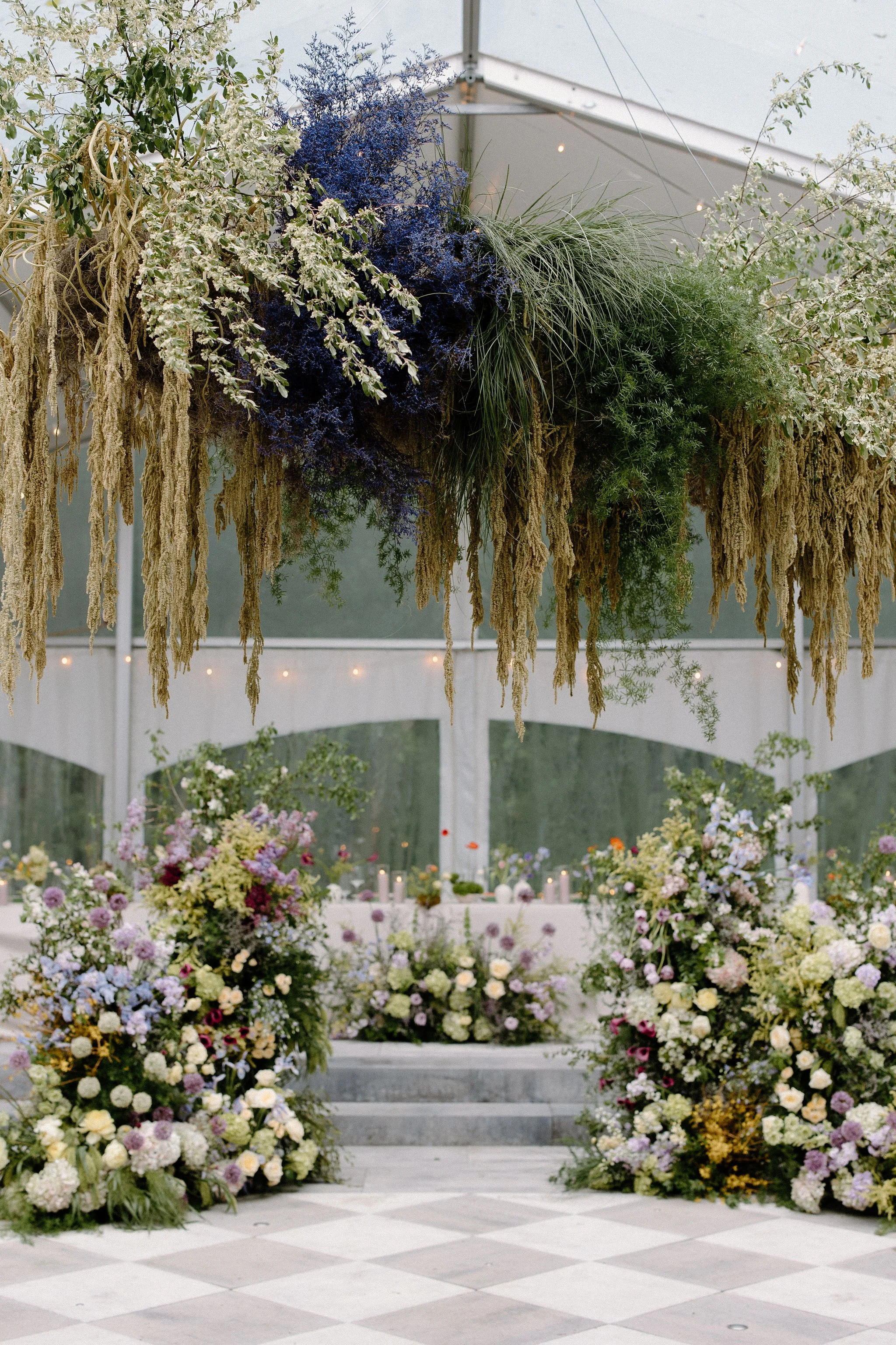  For L+M’s wedding at The Clearing, the floral design by  Forever Wildfield  was nothing short of a masterpiece. To bring a whimsical garden aesthetic inside the clear-top tent, the design team utilized layered, ground-level floral pillars at the alt