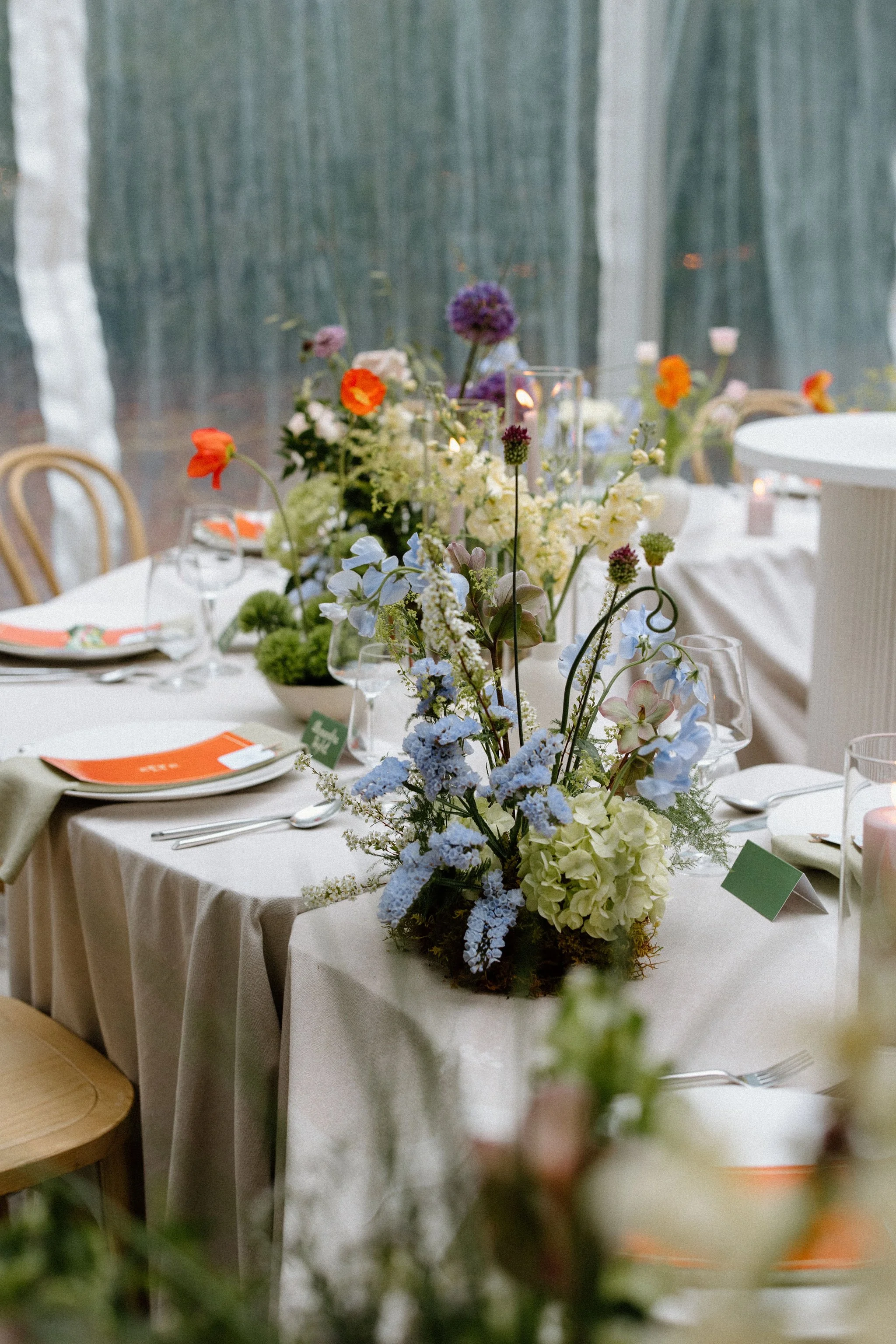  For L+M’s wedding at The Clearing, the floral design by  Forever Wildfield  was nothing short of a masterpiece. To bring a whimsical garden aesthetic inside the clear-top tent, the design team utilized layered, ground-level floral pillars at the alt