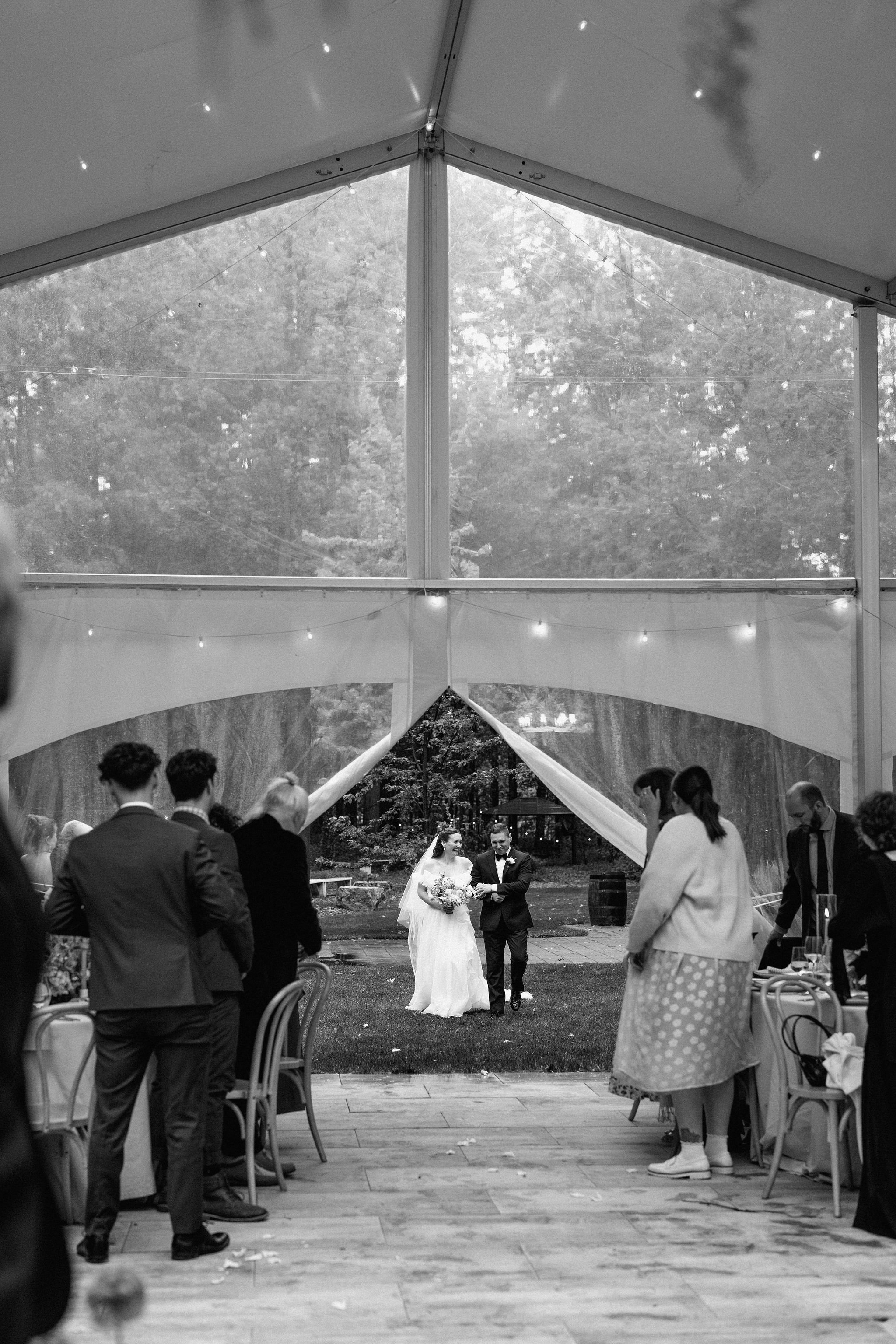  Bride walking up the aisle to meet her groom at the top, under the twinkle lights and clear top tent at The Clearing. 