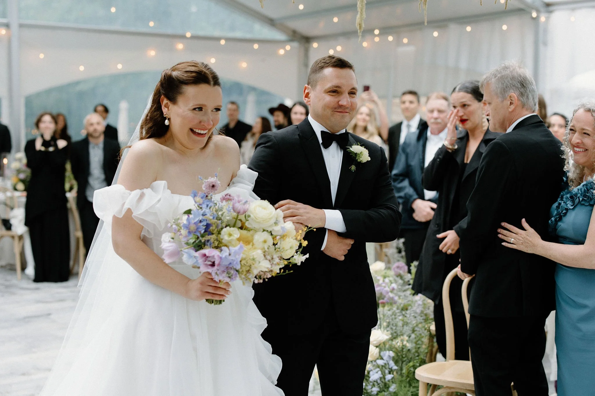  For L+M’s wedding at The Clearing, the floral design by  Forever Wildfield  was nothing short of a masterpiece. To bring a whimsical garden aesthetic inside the clear-top tent, the design team utilized layered, ground-level floral pillars at the alt
