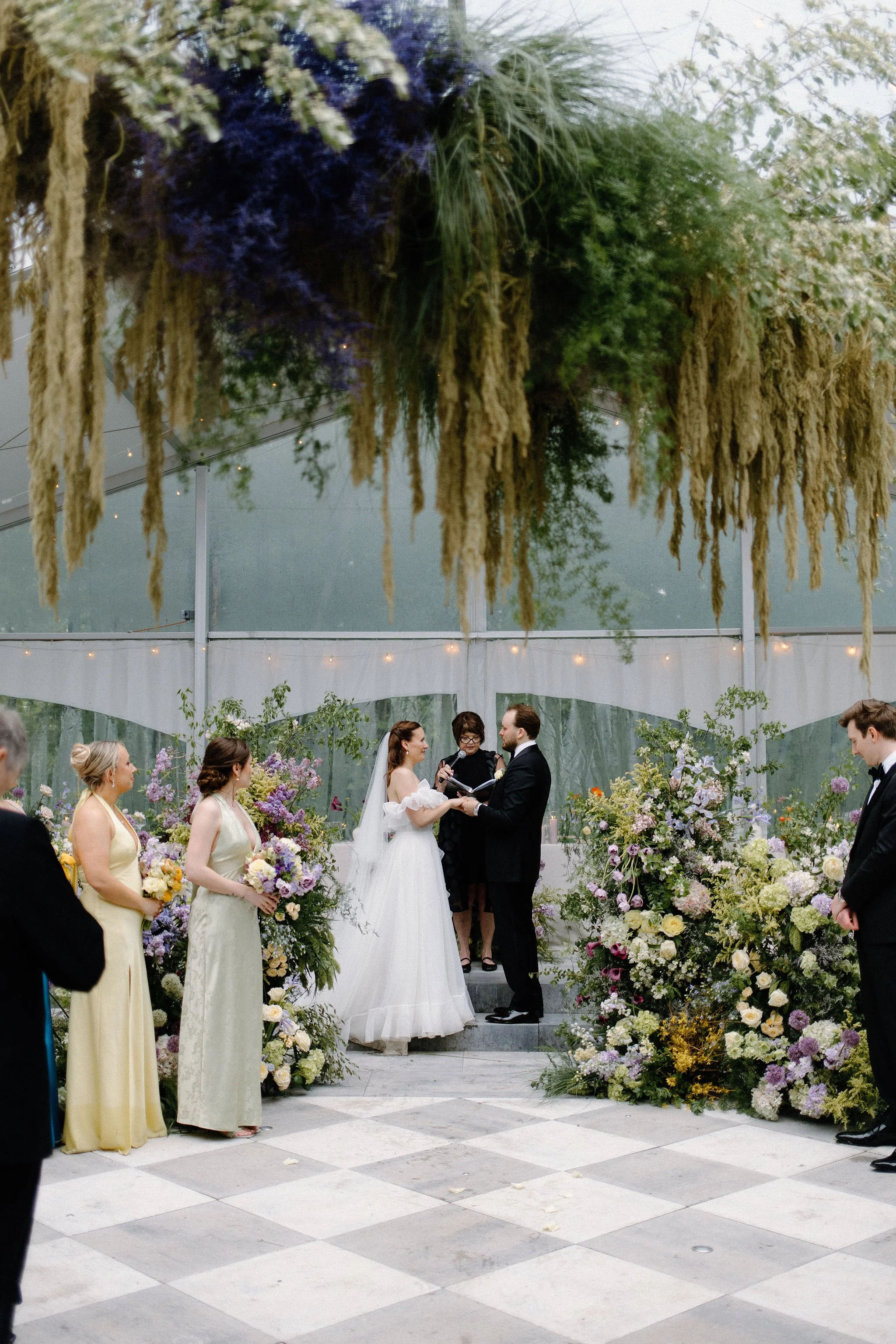  For L+M’s wedding at The Clearing, the floral design by  Forever Wildfield  was nothing short of a masterpiece. To bring a whimsical garden aesthetic inside the clear-top tent, the design team utilized layered, ground-level floral pillars at the alt