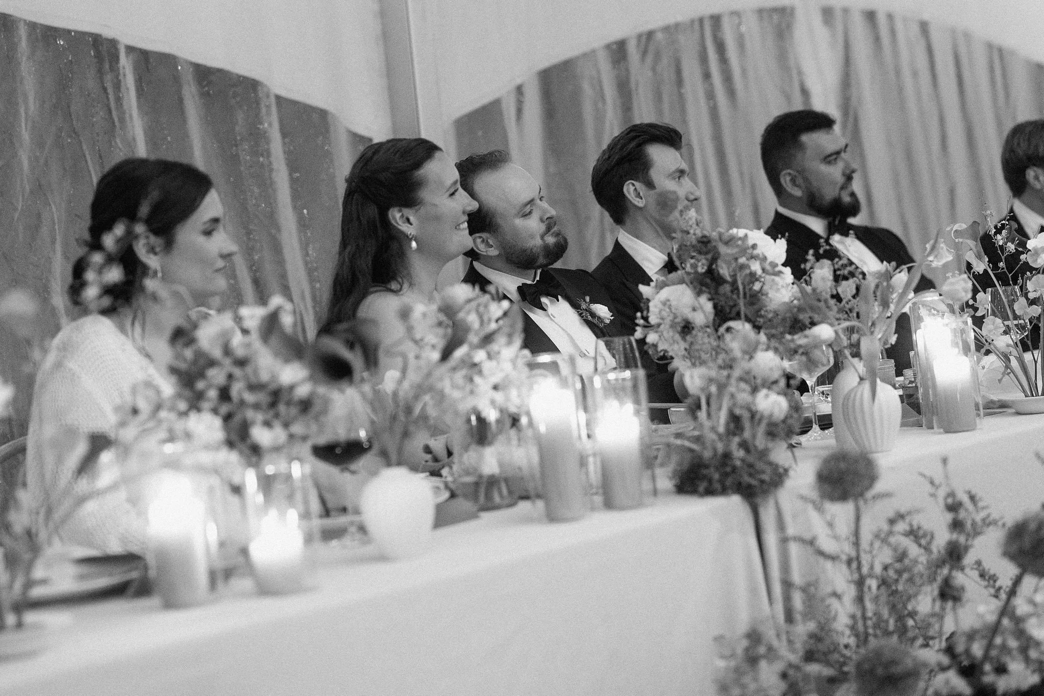  The reception design for this rainy-day wedding at The Clearing was all about movement and texture. Beneath a clear-top tent, striking serpentine curved tables wound through the space, grounded by low-growing floral meadows in shades of sunny yellow