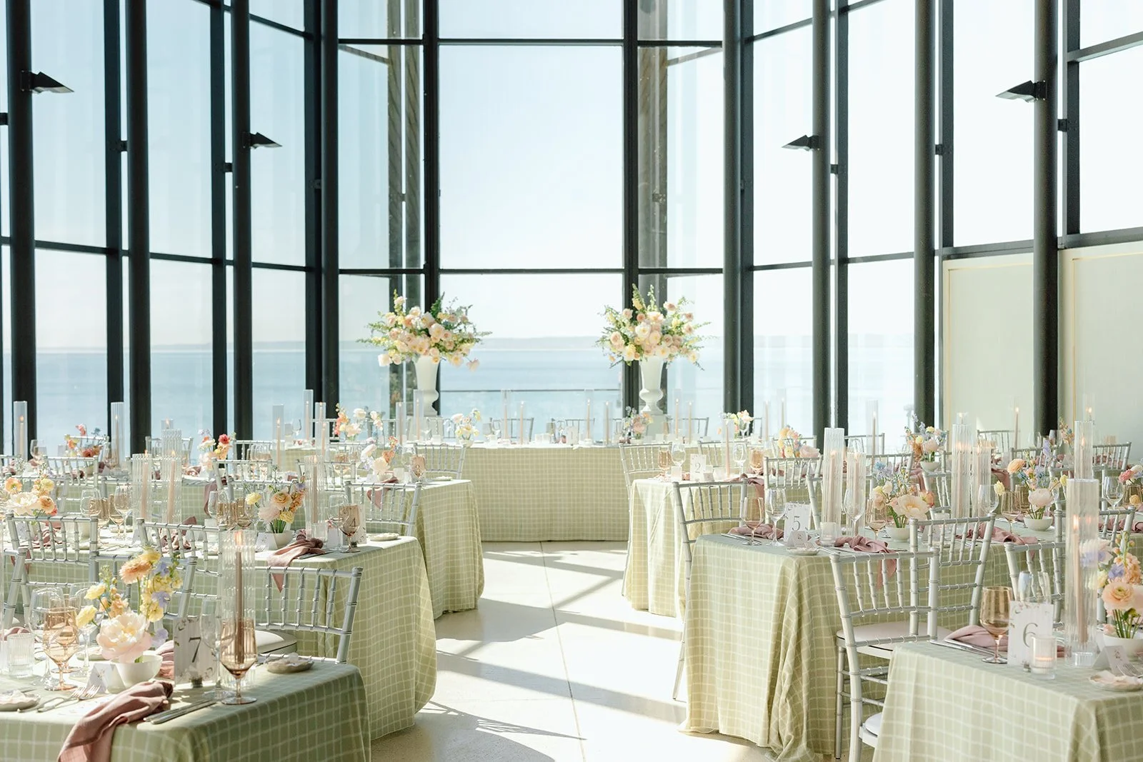  A breathtaking overview of the light-filled dining room at Spencer's at the Waterfront. The architectural clean lines of the black glass frames beautifully contrast with the soft, romantic pastel tones of the tablescapes, creating an airy, garden-es