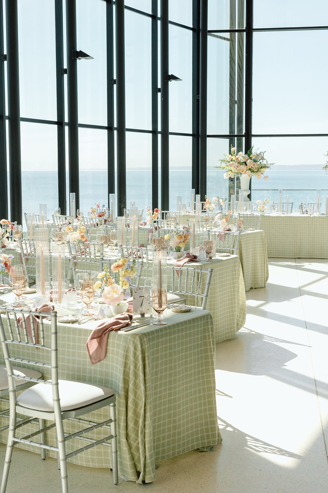  un-drenched bridal shower reception at Spencer's at the Waterfront in Hamilton featuring sage green checkered tablecloths, silver chiavari chairs, and pastel floral centerpieces against floor-to-ceiling glass windows overlooking Lake Ontario. 