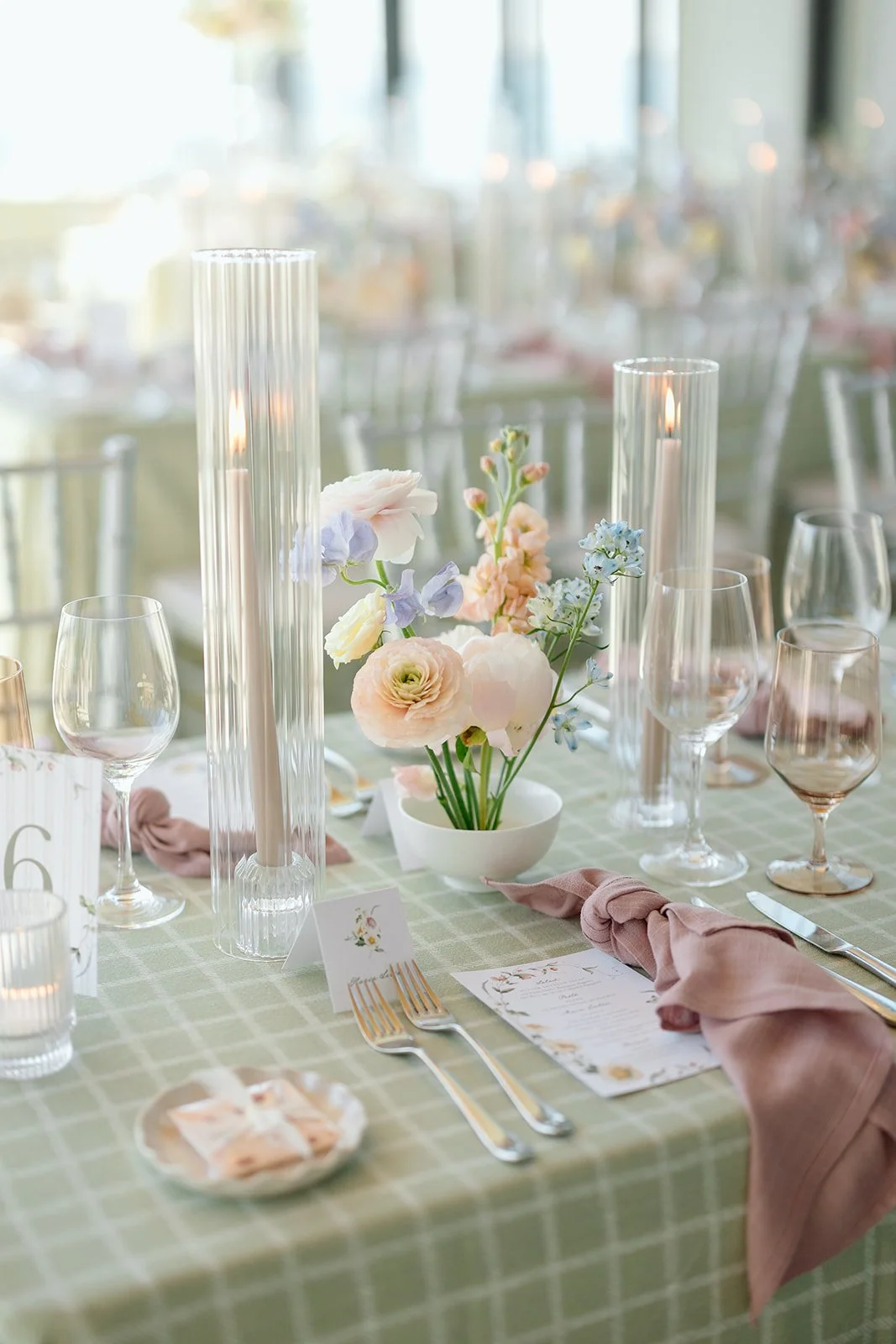  We styled the tables with a refreshing sage green and white checkered linen, paired beautifully with dusty mauve linen napkins knotted effortlessly over custom floral-accented menus. 