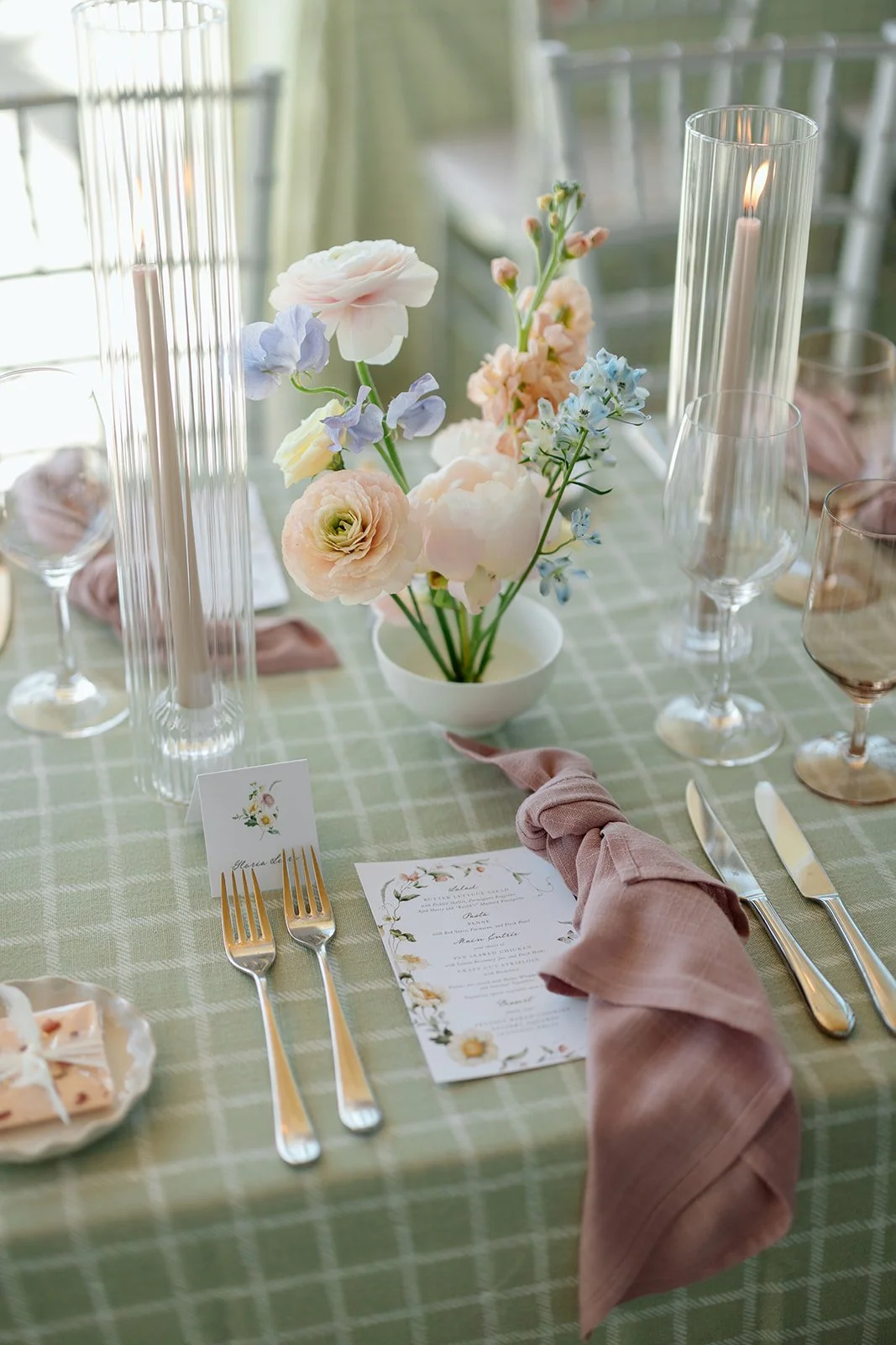  A close-up of the place setting featuring the sage checkered linen, dusty rose knotted napkin, custom menu, and delicate floral centerpiece. 
