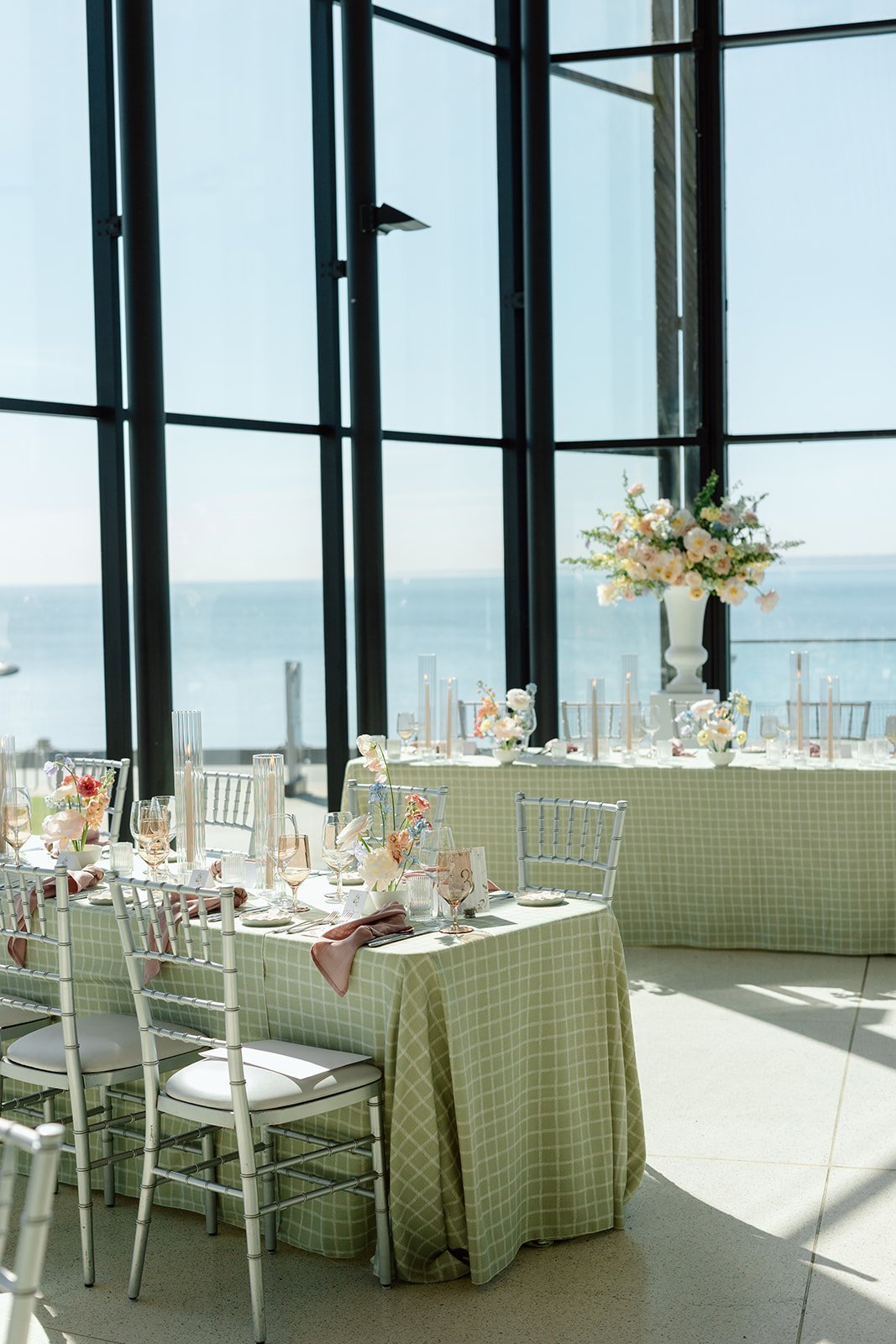  This perspective highlights how the natural midday sun interacts with our design choices. The metallic sheen of the silver chiavari chairs elevates the casual elegance of the gingham-style plaid linens. 