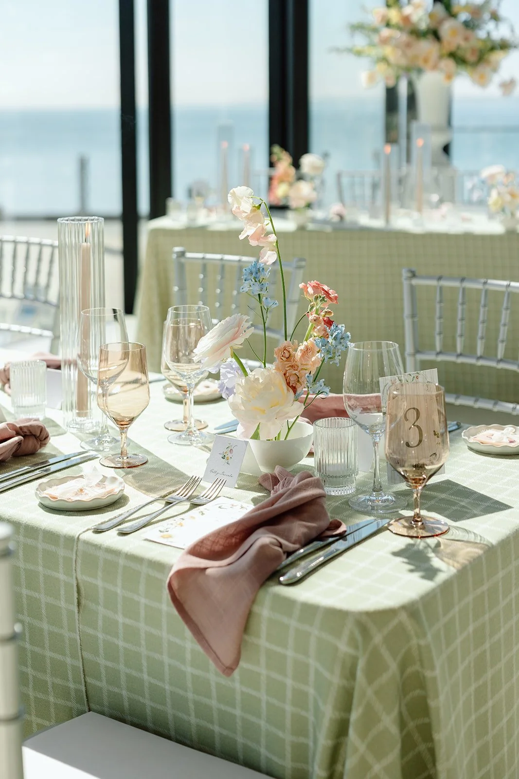  Long estate table wedding setup with a sage green tablecloth, dusty mauve napkins, flickering taper candles in ribbed glass sleeves, and lake views at Spencer’s Burlington. 