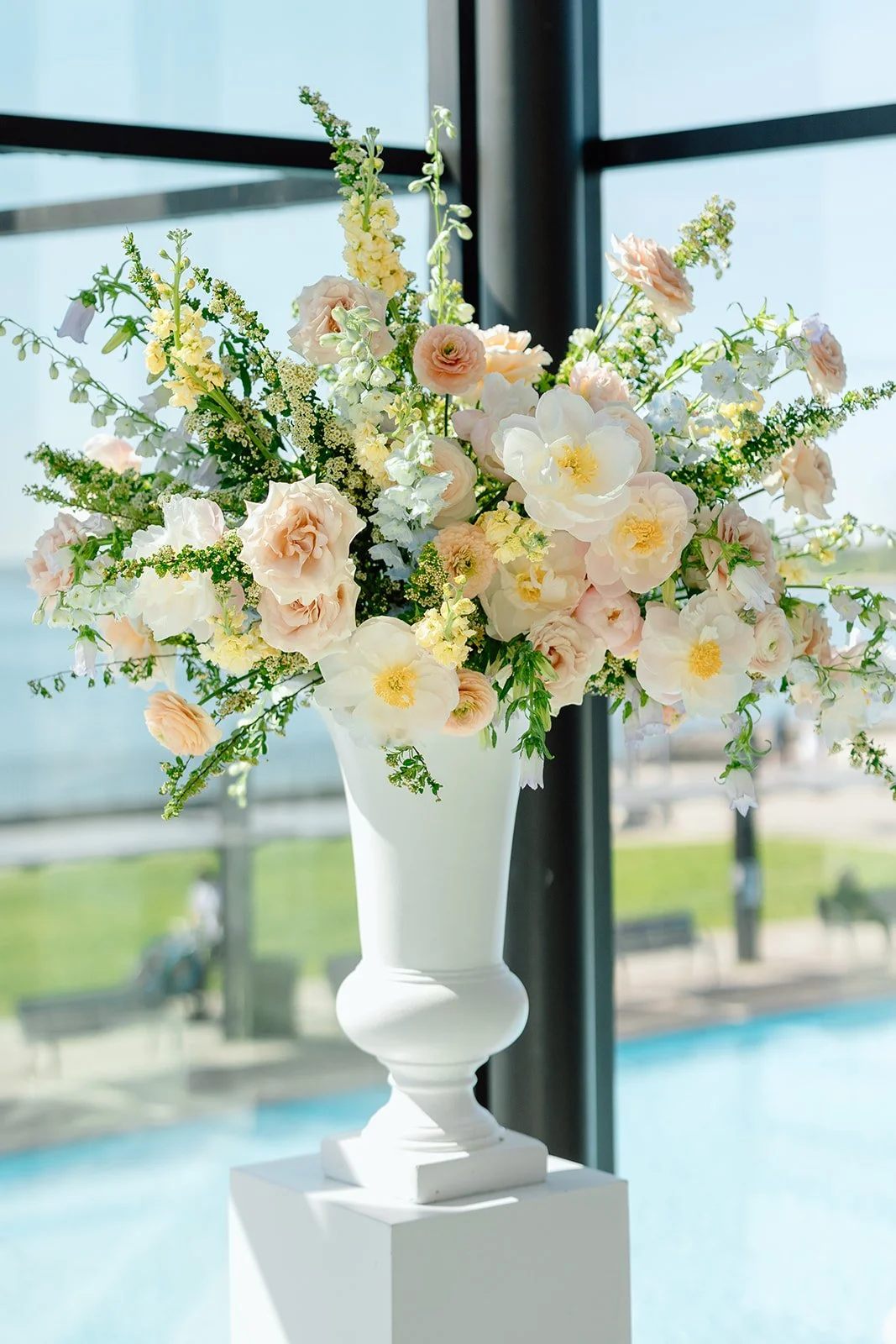  To draw the eye up toward the beautiful Lake Ontario views, we lined estate tables with tall, ribbed glass hurricane candle sleeves and introduced towering floral urns. Curated by Simply Elegant by Emma. 