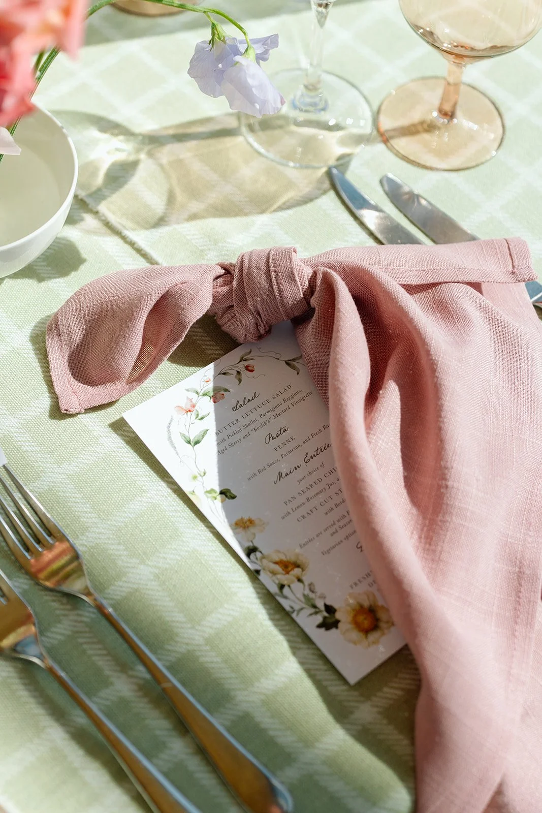  We broke away from traditional all-white decor by introducing a refreshing sage green and white checkered linen. This was layered with rich, dusty rose linen napkins knotted over custom-designed botanical menus. 