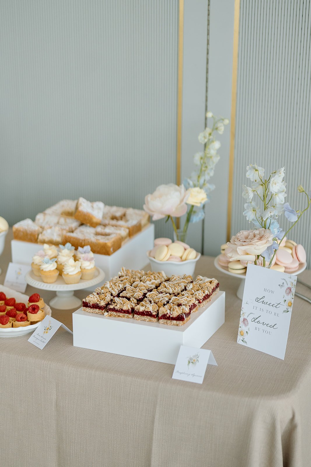  A beautifully styled dessert table featuring artisanal raspberry crumble bars on sleek white display risers, adding a luxurious touch to the sweet station.  