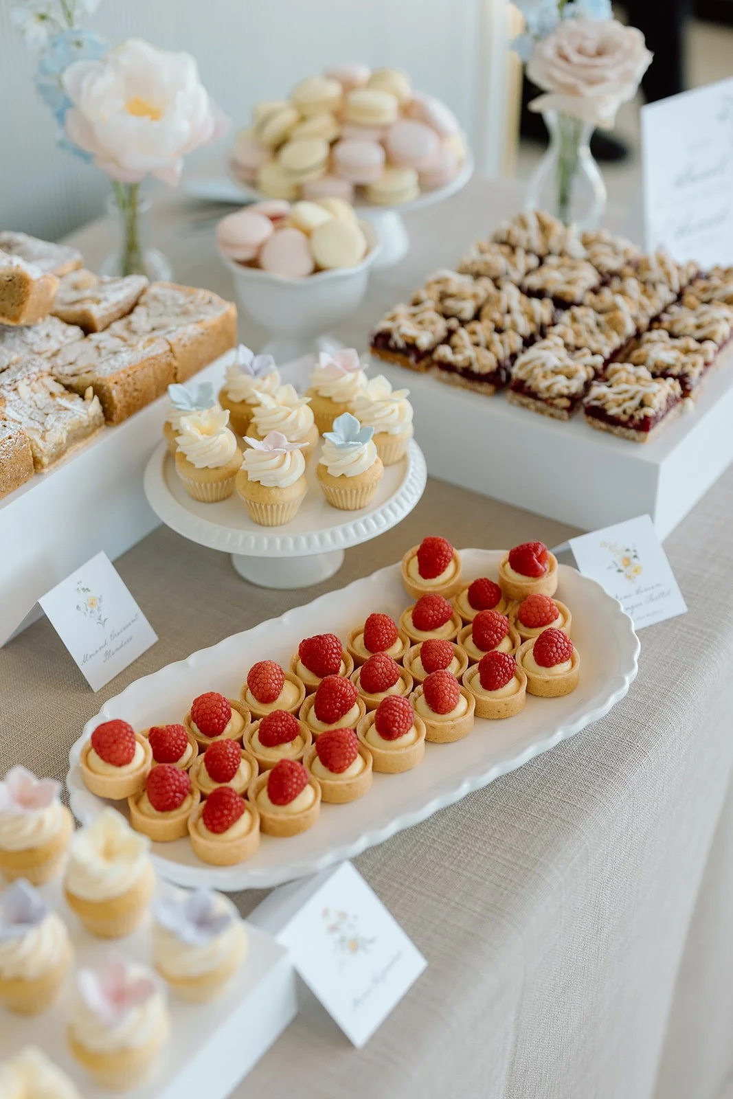  A curated dessert table featured gourmet treats, including perfectly drizzled berry crumble bars alongside classic French macarons. By The Dessert Room 