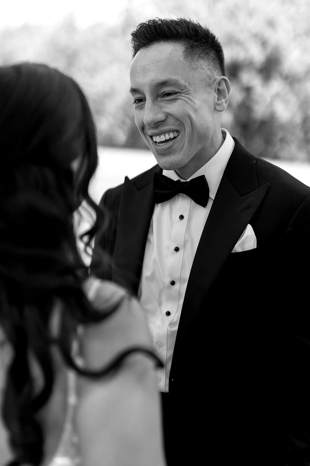  Black and white portrait of a smiling groom in a classic tuxedo at a Niagara-on-the-Lake wedding venue, captured by Paula Visco Photography. 