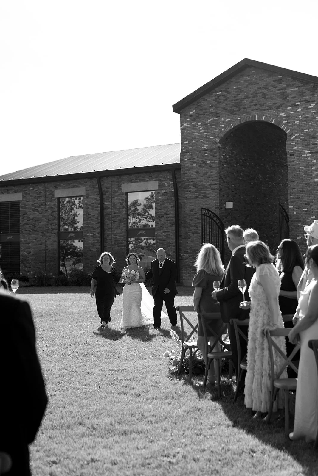  Bride is walked down the aisle by her mother and father to her from waiting under the Chuppah during their vineyard side ceremony at The Hare Wine Co. 