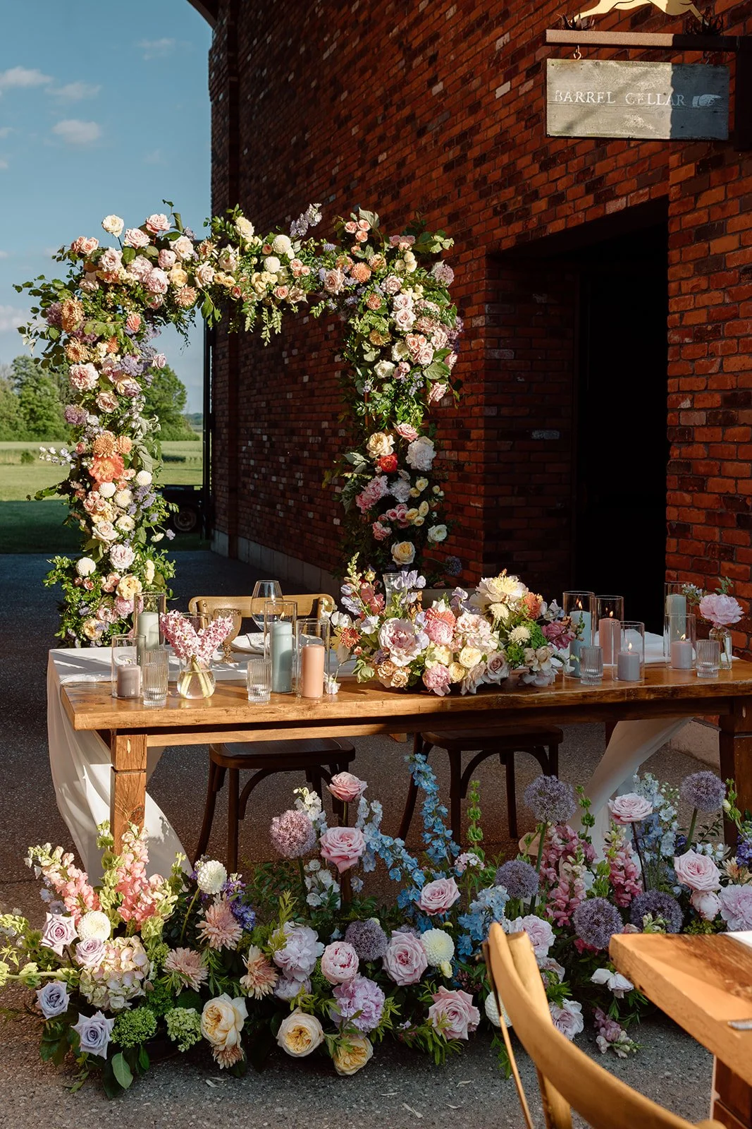  Modern wooden wedding arch covered in colorful pastel pink, orange, and purple flowers. 