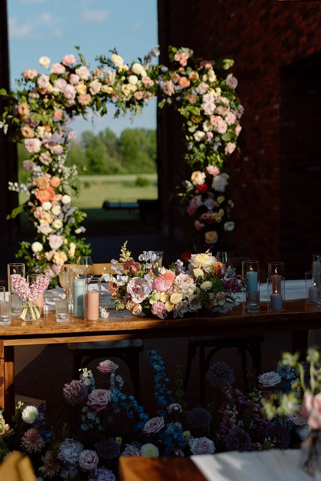  Romantic wedding tablescape with a white chiffon runner, pastel bud vase florals by threads &amp; blooms, pillared candles, and crossback chair 