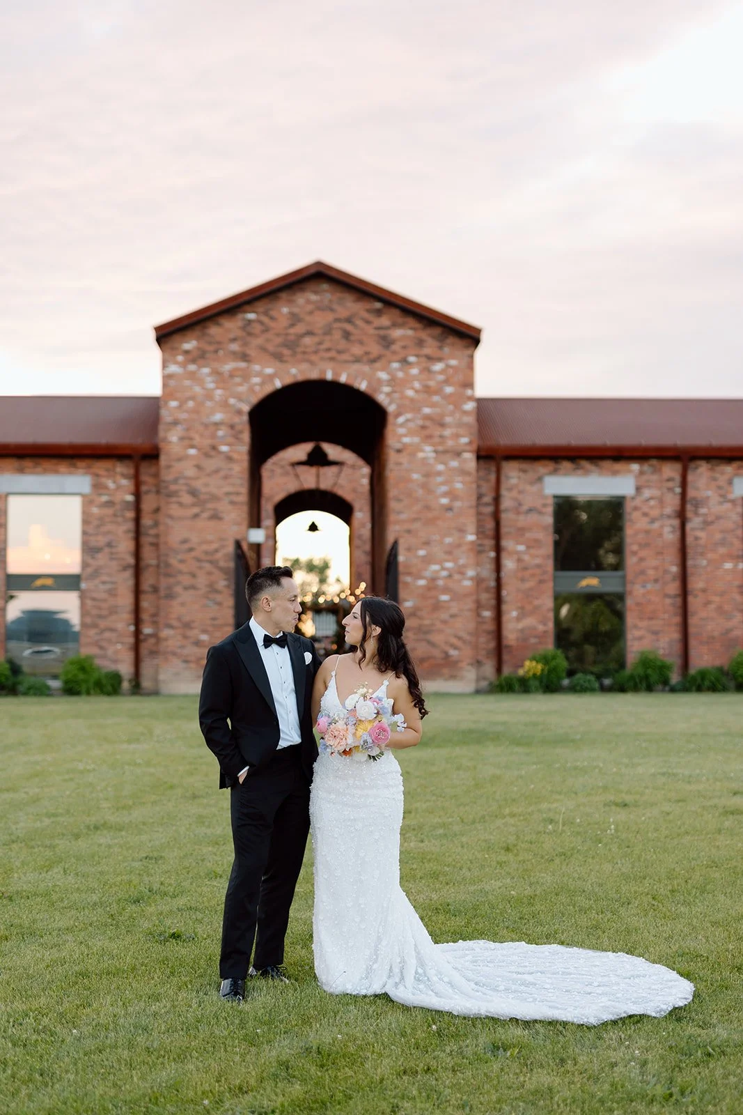  Newlyweds walking together on the property of a Niagara-on-the-Lake winery venue. The Hare Wine co.   