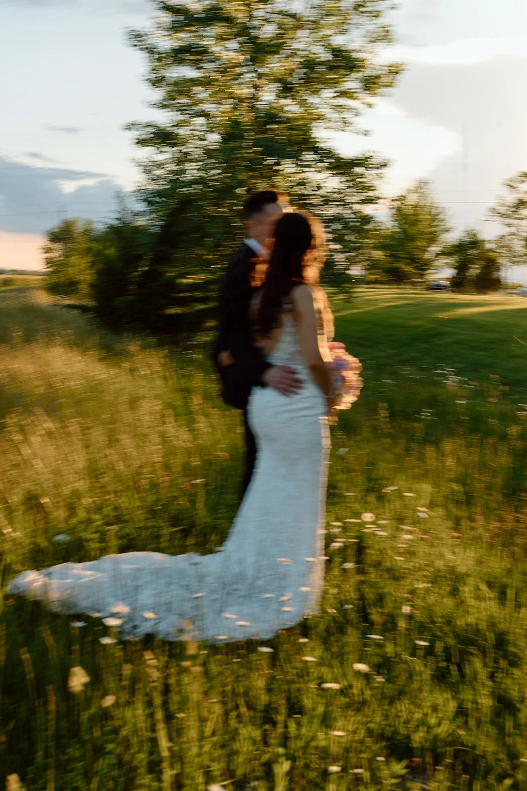  Artistic motion-blur wedding photography of a bride and groom walking through a field at golden hour in Niagara-on-the-Lake. 