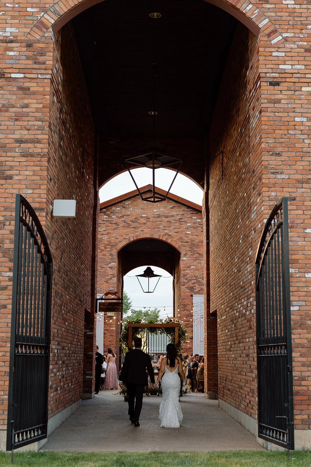  Bride and groom walking through the dramatic brick archways at dusk for their reception entrance at The Hare Wine Co, planned by Lindsay Plank Events. 