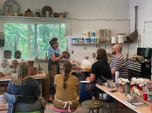 Four students gathered around a teacher presenting a lesson in pottery.