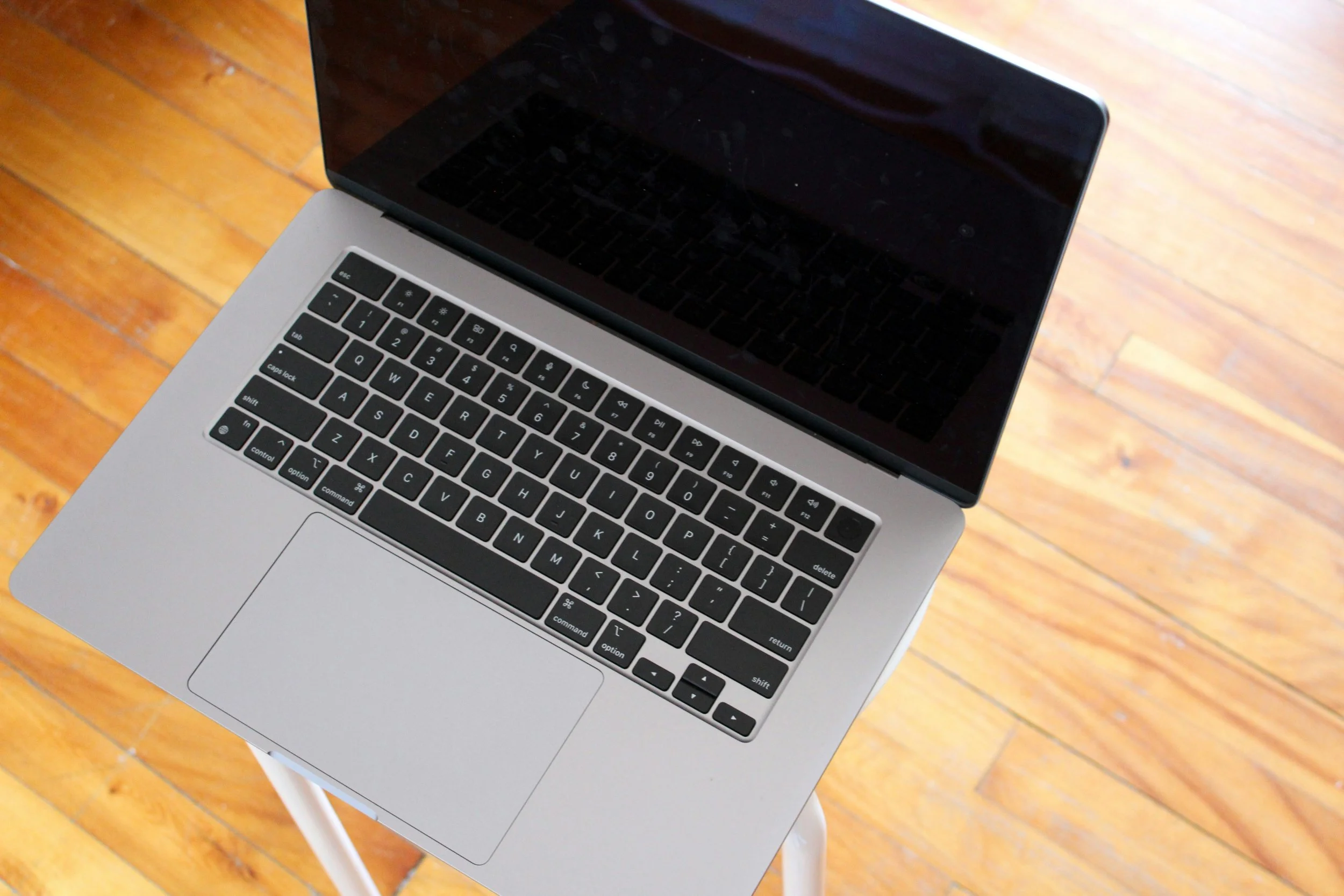 Top view of a silver laptop with black keyboard on a small white table, hardwood floor underneath.