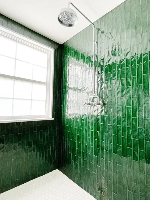 Green tiled shower with a large window and a ceiling-mounted showerhead.