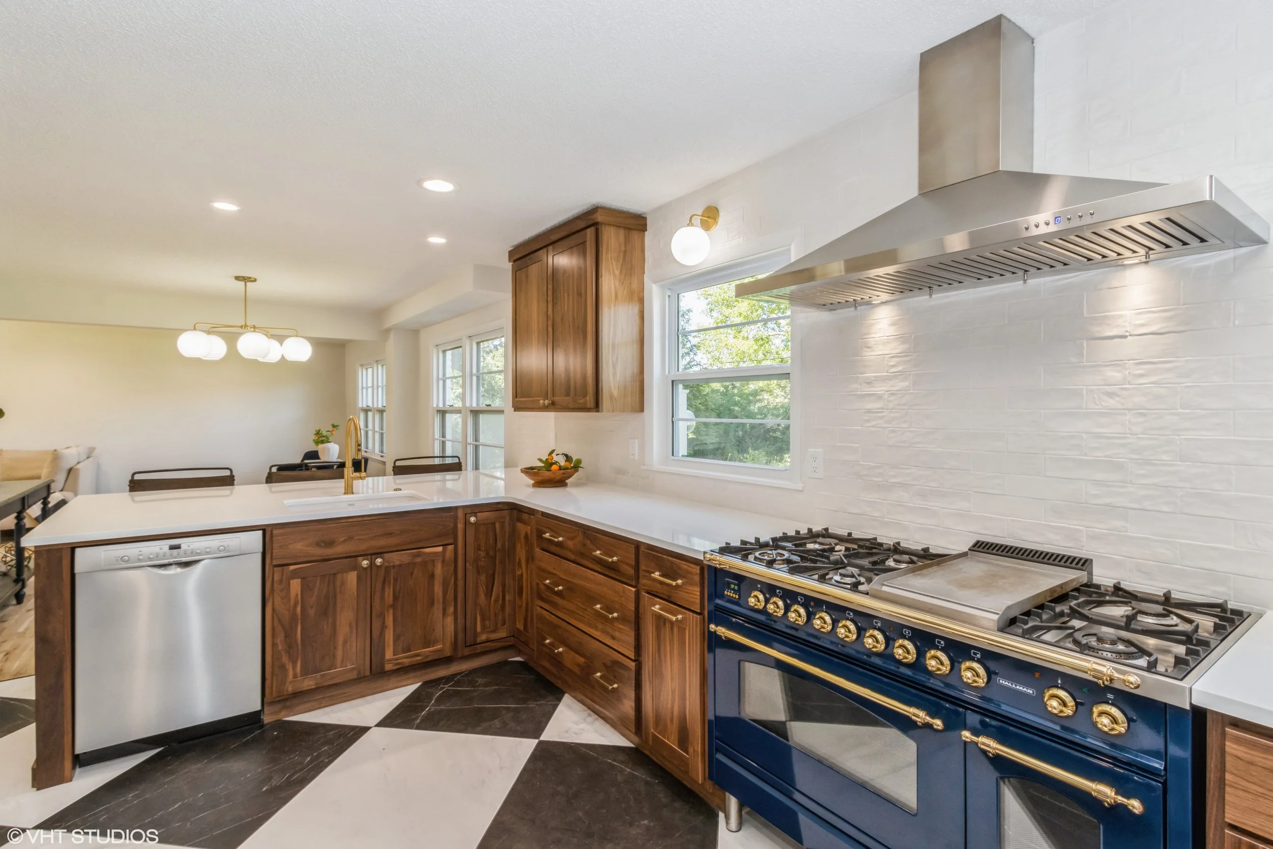 Kitchen with wooden cabinets, stainless steel and blue appliances, white countertops, and black and white checkered floor tiles.