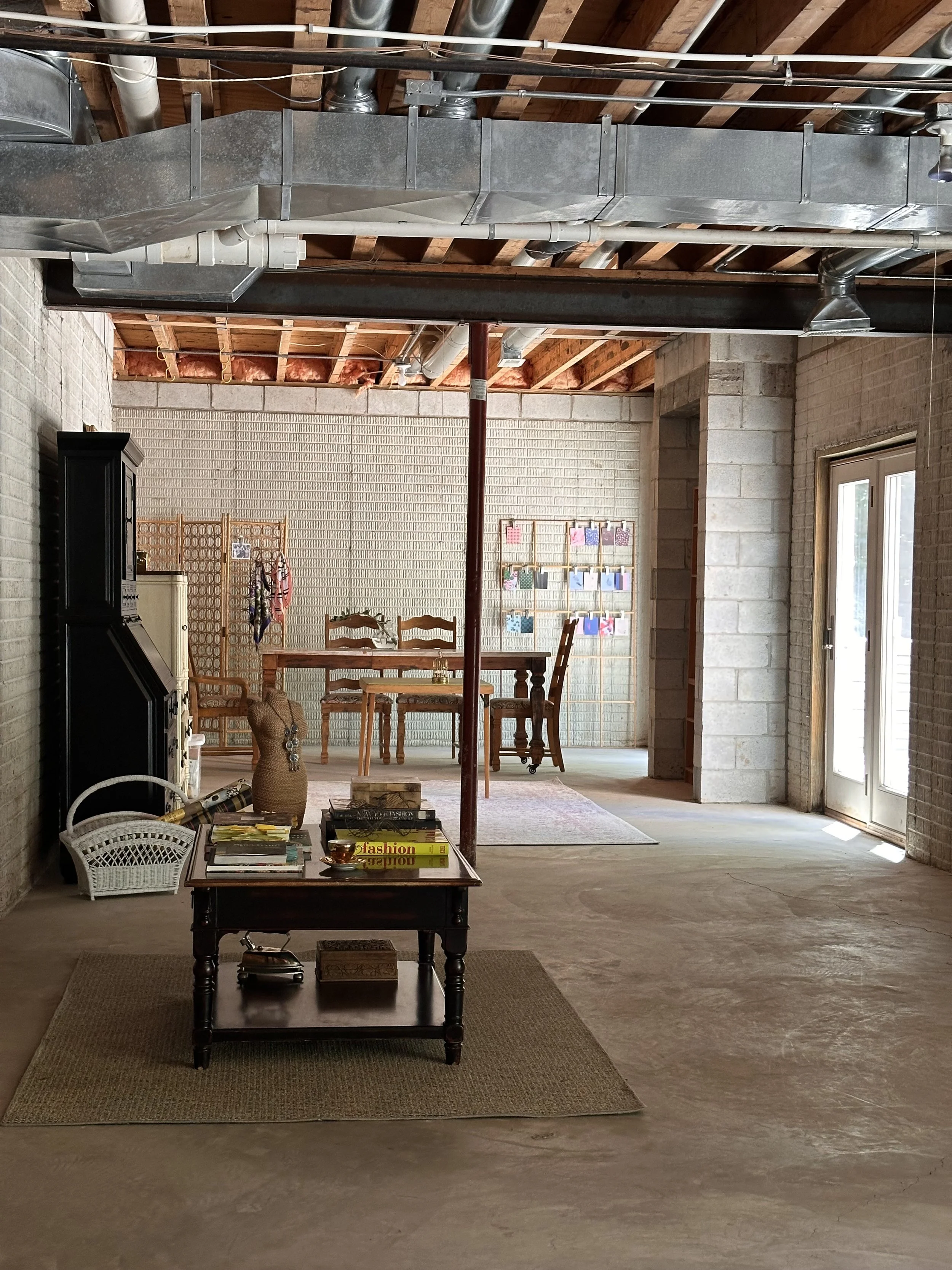 An artistically designed angle of a creative studio in th ebasement with light pouring in from walkouts, a collection on fashion and design coffe table books and tastefully placed vintage furniture giving the space an Architectural Digest standard