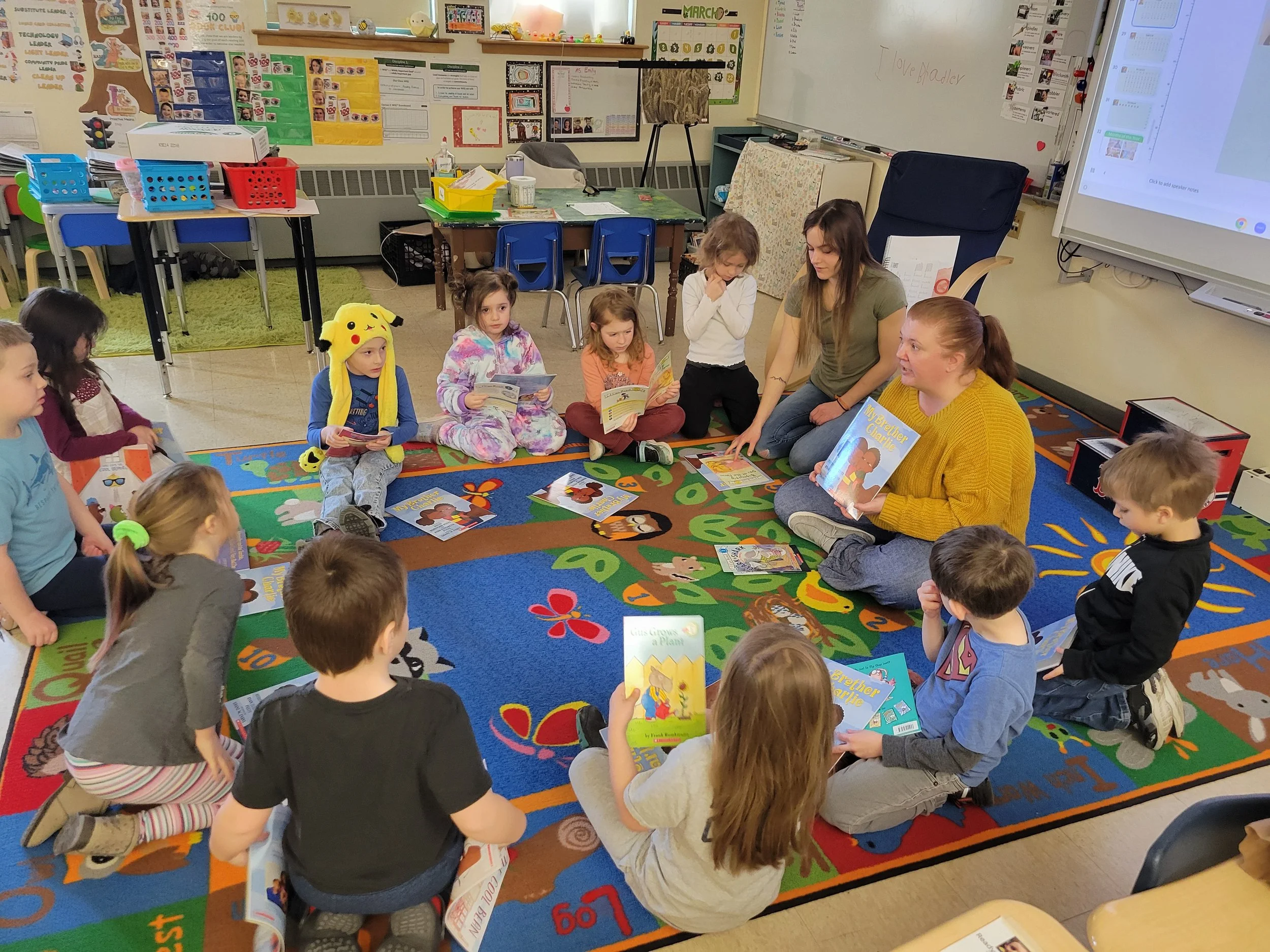 Children sit in a classroom reading circle as an educator shares a book with the group.